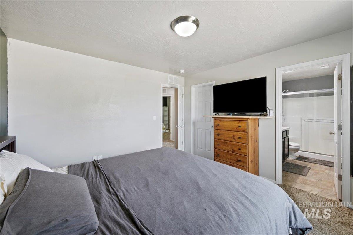 Master Bedroom with carpet, a textured ceiling, ensuite bath, and stone finish floors