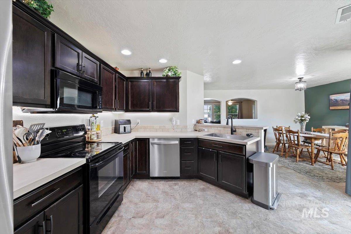 Kitchen with black appliances, light countertops, a peninsula, dark brown cabinetry, and a textured ceiling