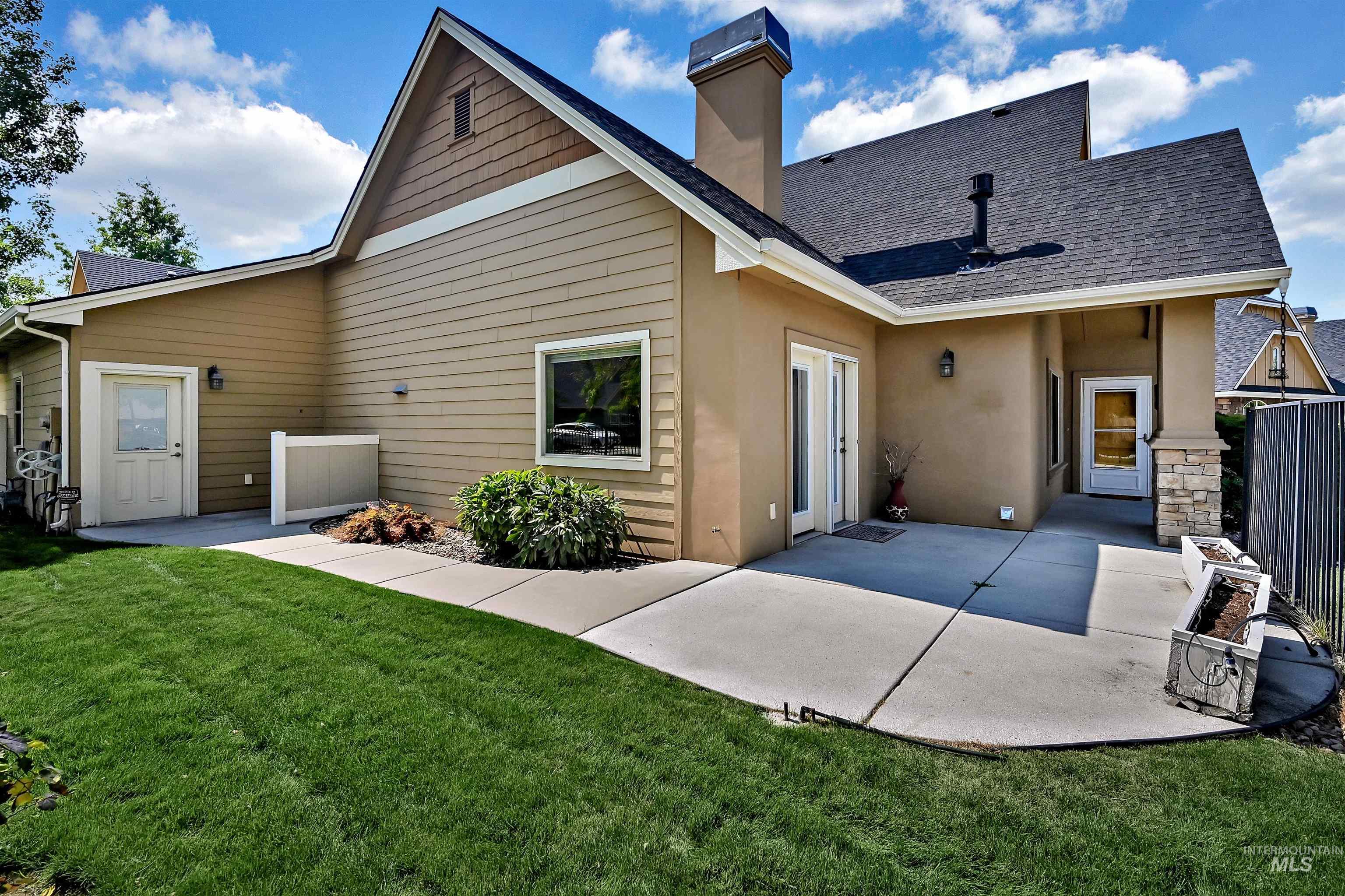 Rear view of property with a shingled roof, a patio area, a lawn, a chimney, and stucco siding