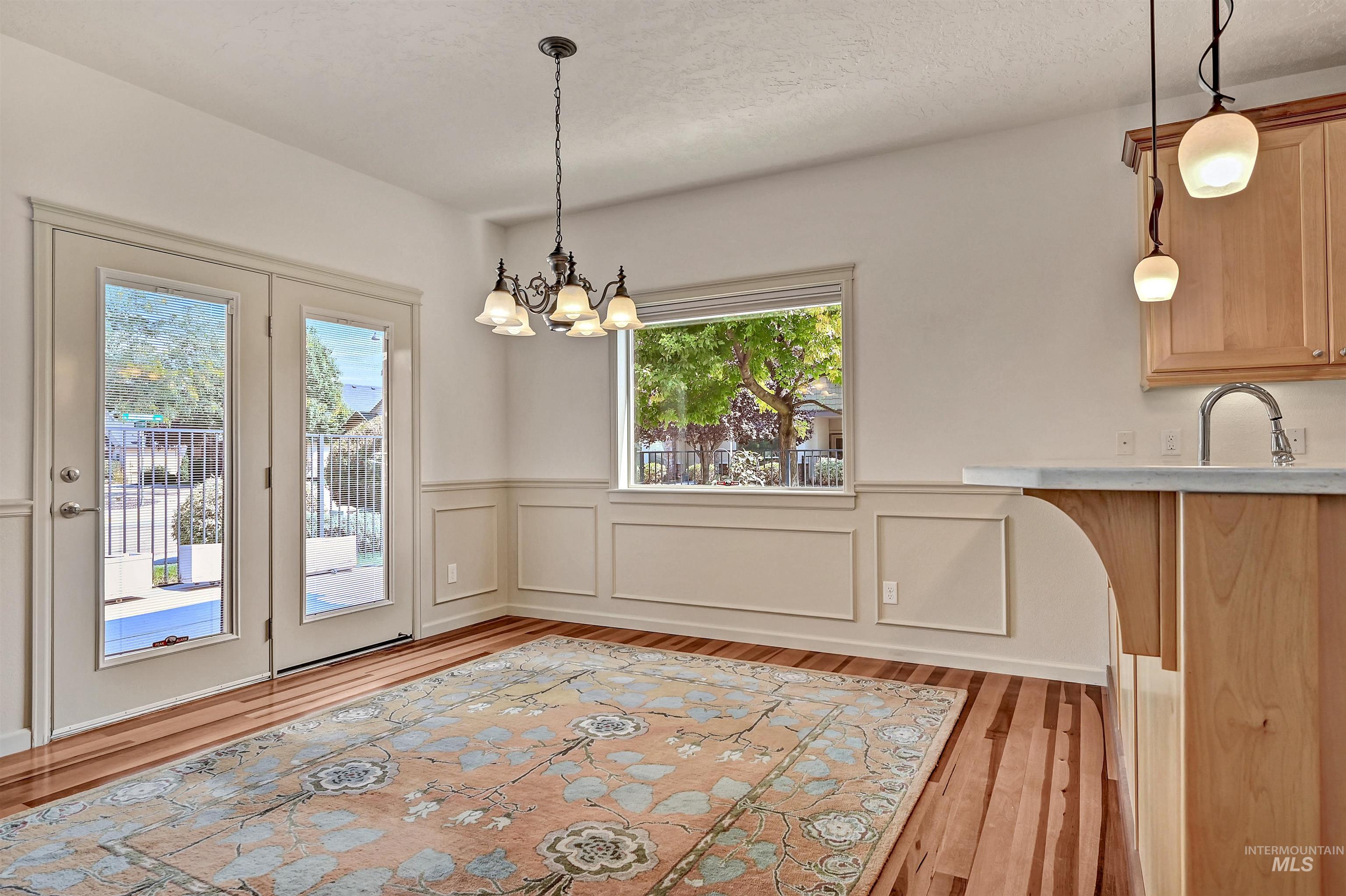 Dining room with a wainscoted wall, a decorative wall, light wood-type flooring, a chandelier, and a textured ceiling