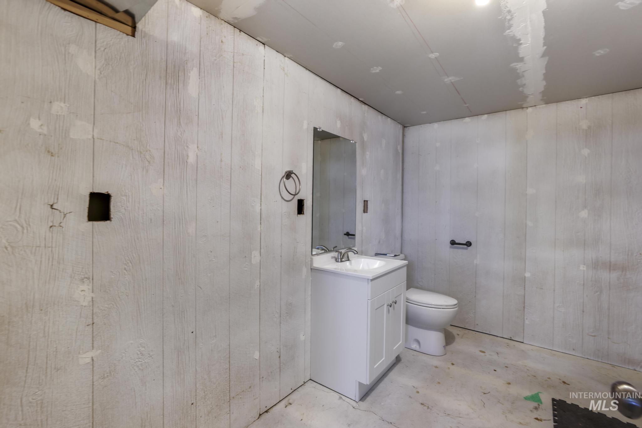 Half bath with vanity, wooden walls, and unfinished concrete flooring