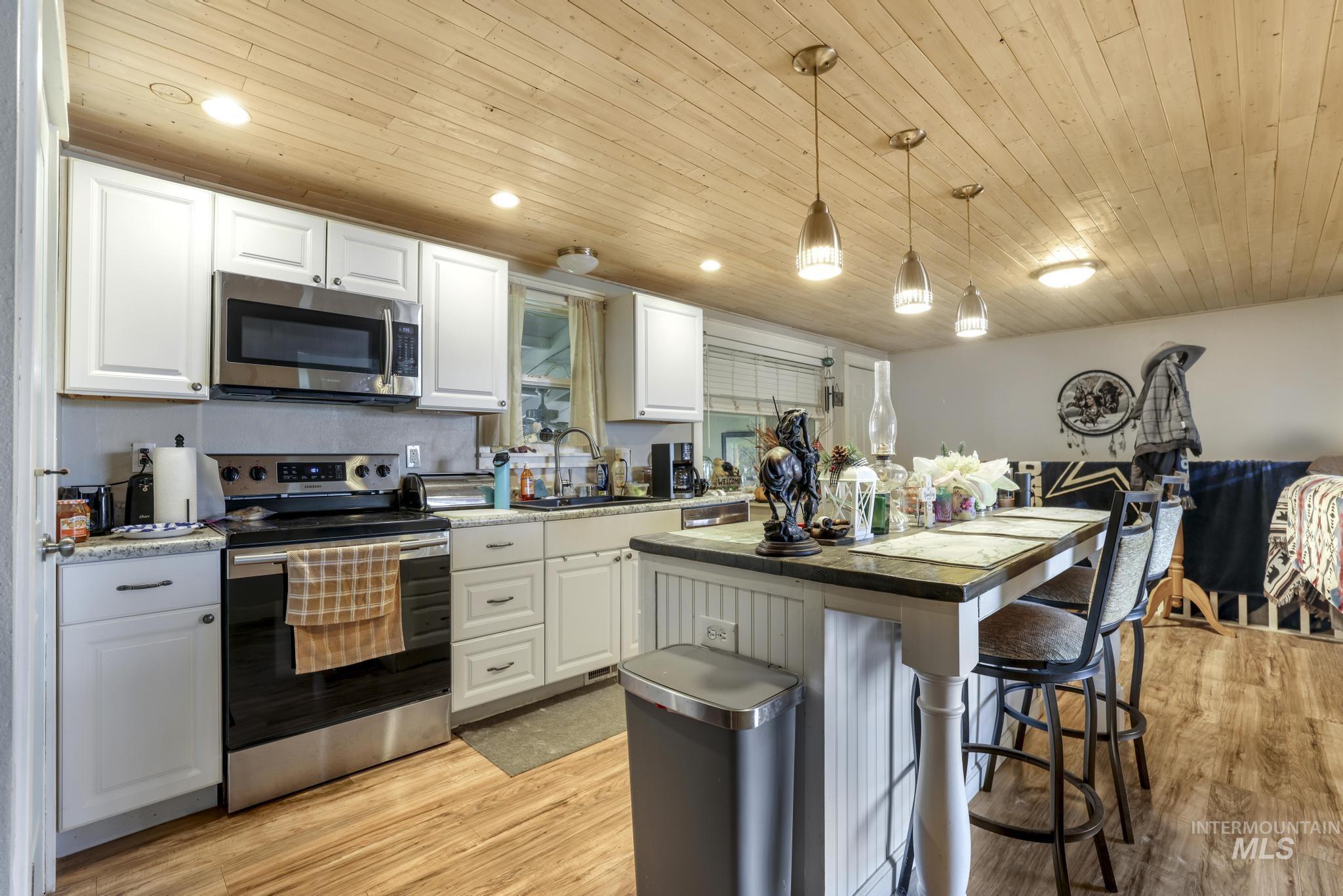 Kitchen with appliances with stainless steel finishes, a breakfast bar area, white cabinetry, light wood finished floors, and a center island
