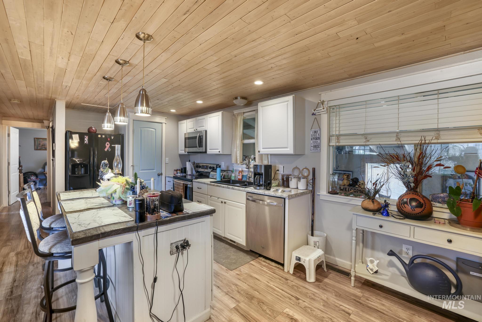 Kitchen featuring white cabinets, light wood-style floors, wood ceiling, appliances with stainless steel finishes, and a kitchen bar