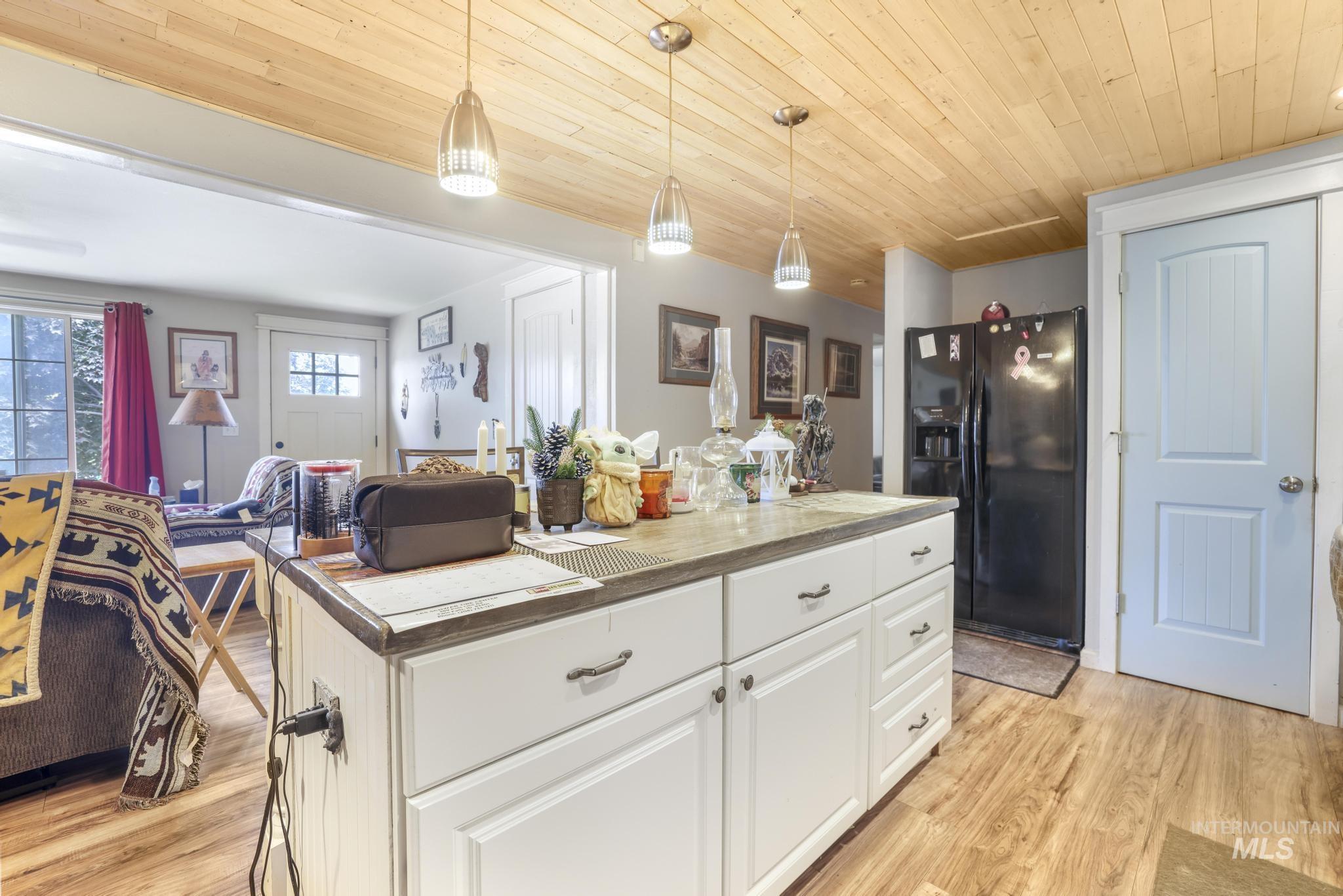 Kitchen featuring decorative light fixtures, black refrigerator with ice dispenser, light wood finished floors, white cabinets, and wooden ceiling