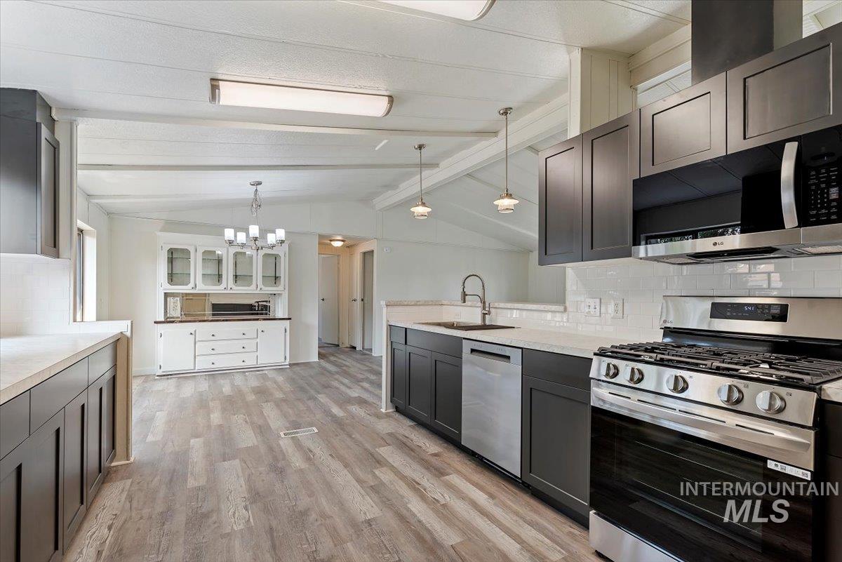 Kitchen featuring decorative backsplash, appliances with stainless steel finishes, light wood-style flooring, hanging light fixtures, and glass insert cabinets