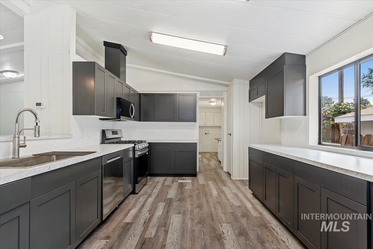 Kitchen with lofted ceiling, light countertops, appliances with stainless steel finishes, and light wood-style floors