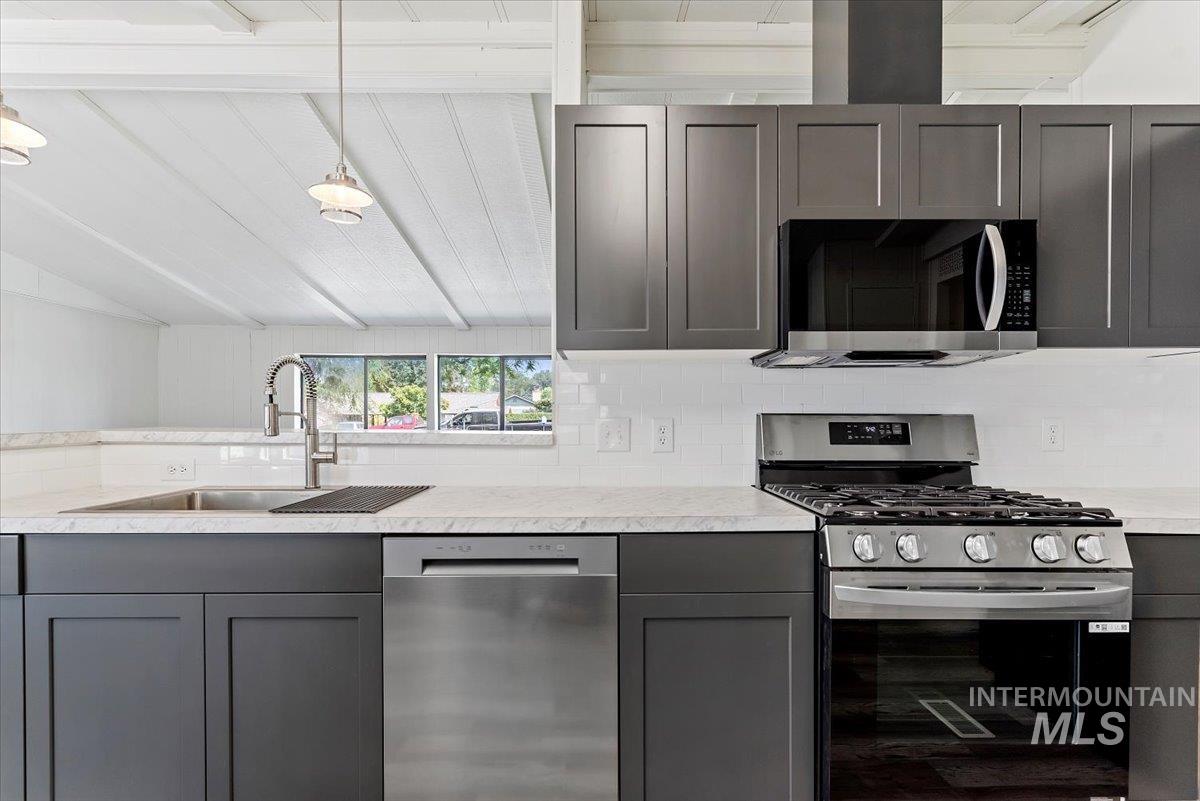 Kitchen featuring appliances with stainless steel finishes, gray cabinets, decorative backsplash, and pendant lighting