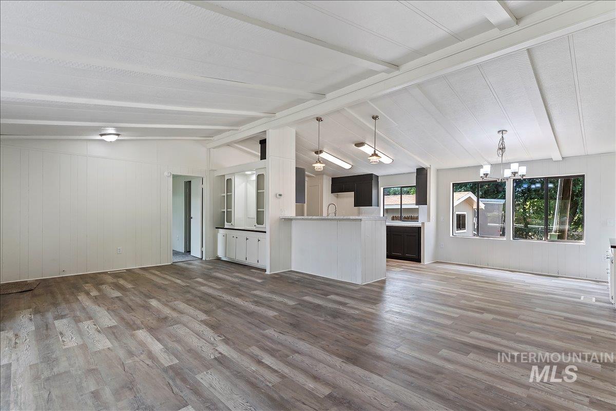 Unfurnished living room with wood walls, dark wood-style flooring, and a chandelier