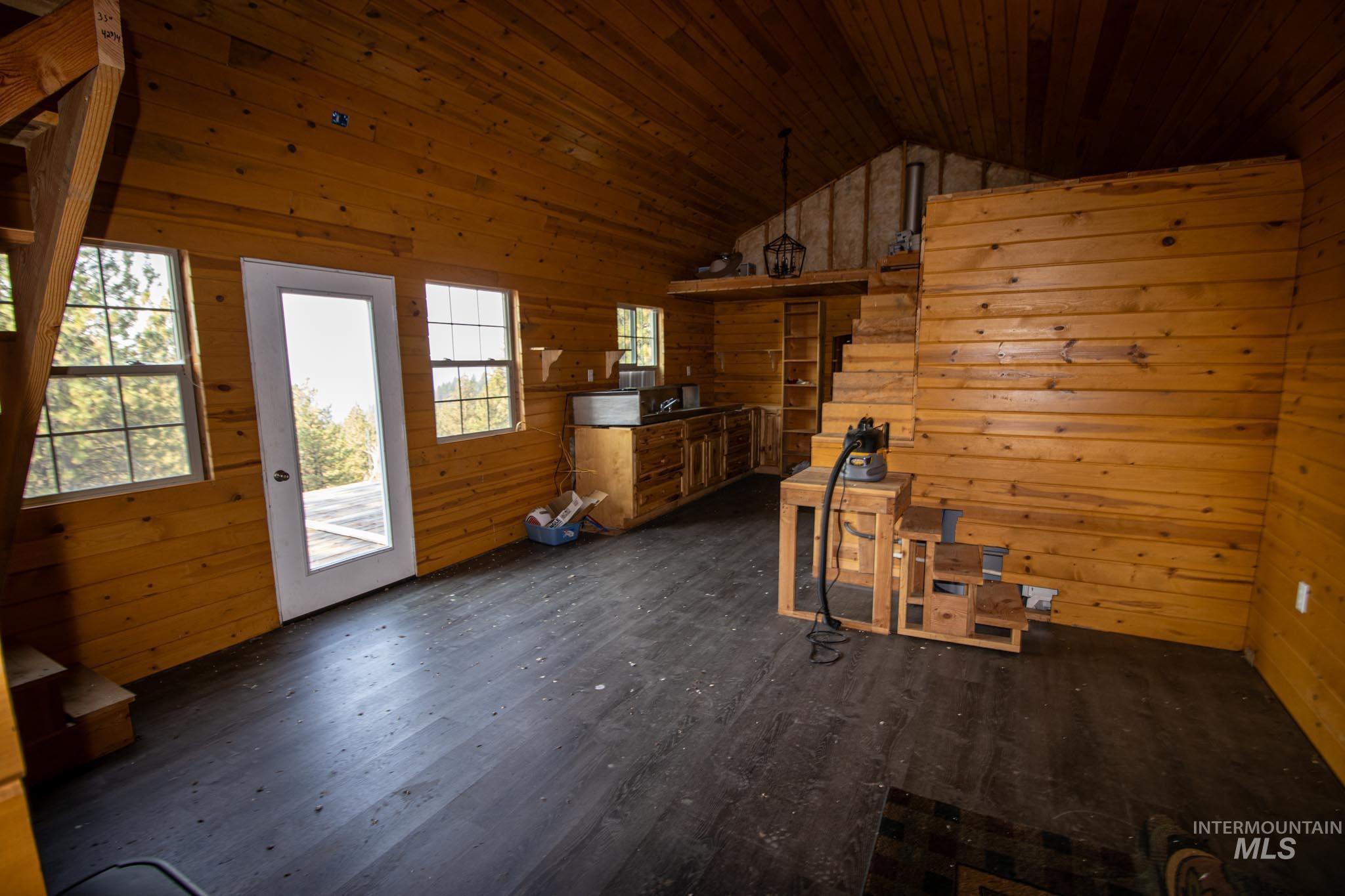 Unfurnished living room featuring wooden walls, dark wood finished floors, wooden ceiling, and high vaulted ceiling