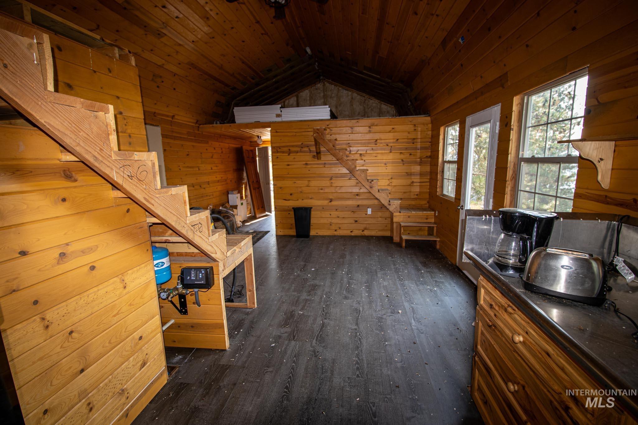 Unfurnished living room featuring wood walls, dark wood-type flooring, stairway, vaulted ceiling, and wood ceiling