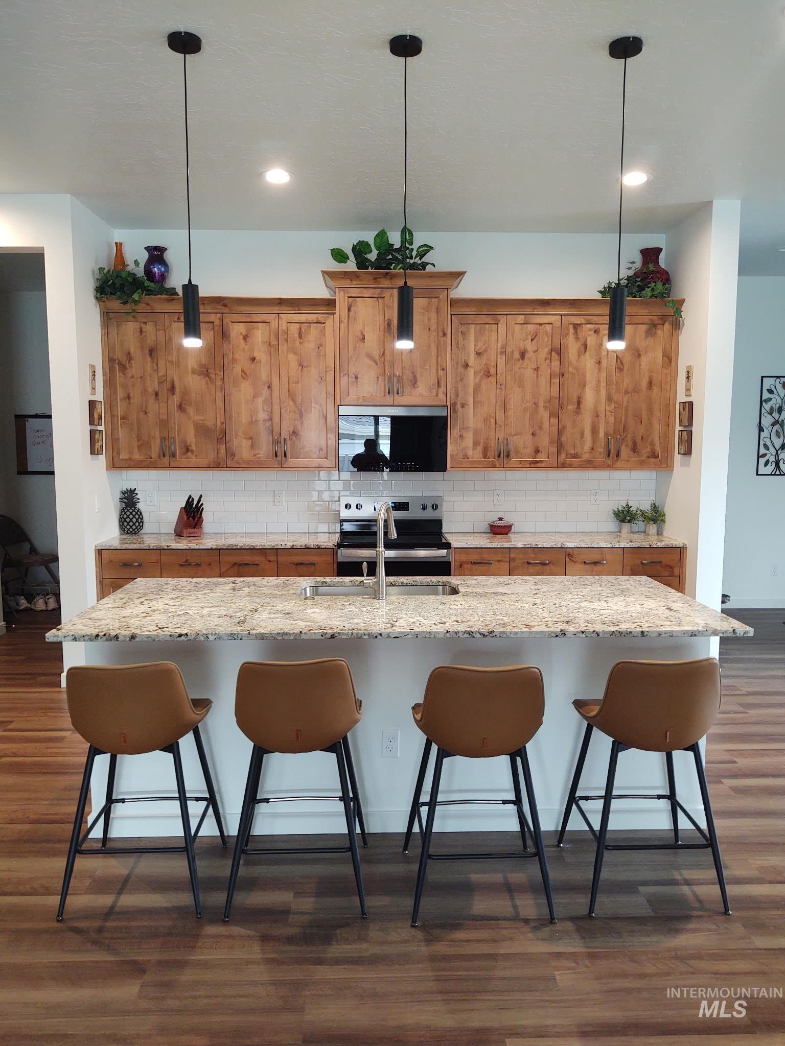 Kitchen featuring a kitchen bar, brown cabinets, appliances with stainless steel finishes, and dark wood-style flooring