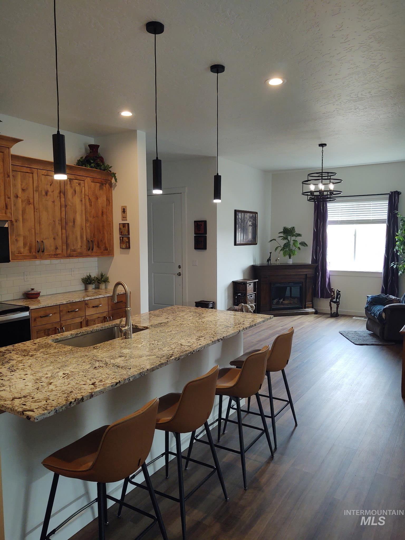 Kitchen with a kitchen bar, brown cabinets, decorative light fixtures, light stone counters, and recessed lighting