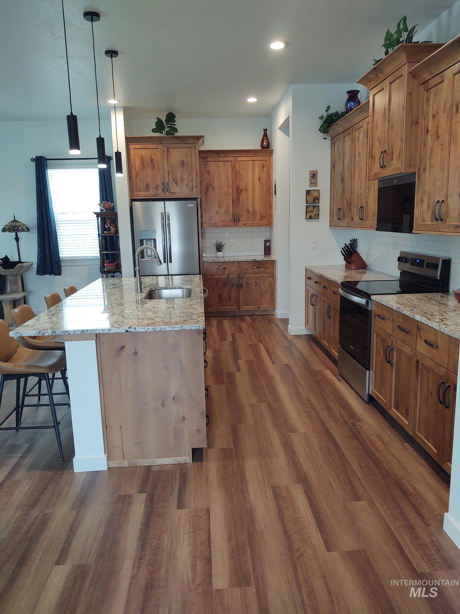 Kitchen featuring stainless steel appliances, light stone counters, brown cabinets, pendant lighting, and recessed lighting