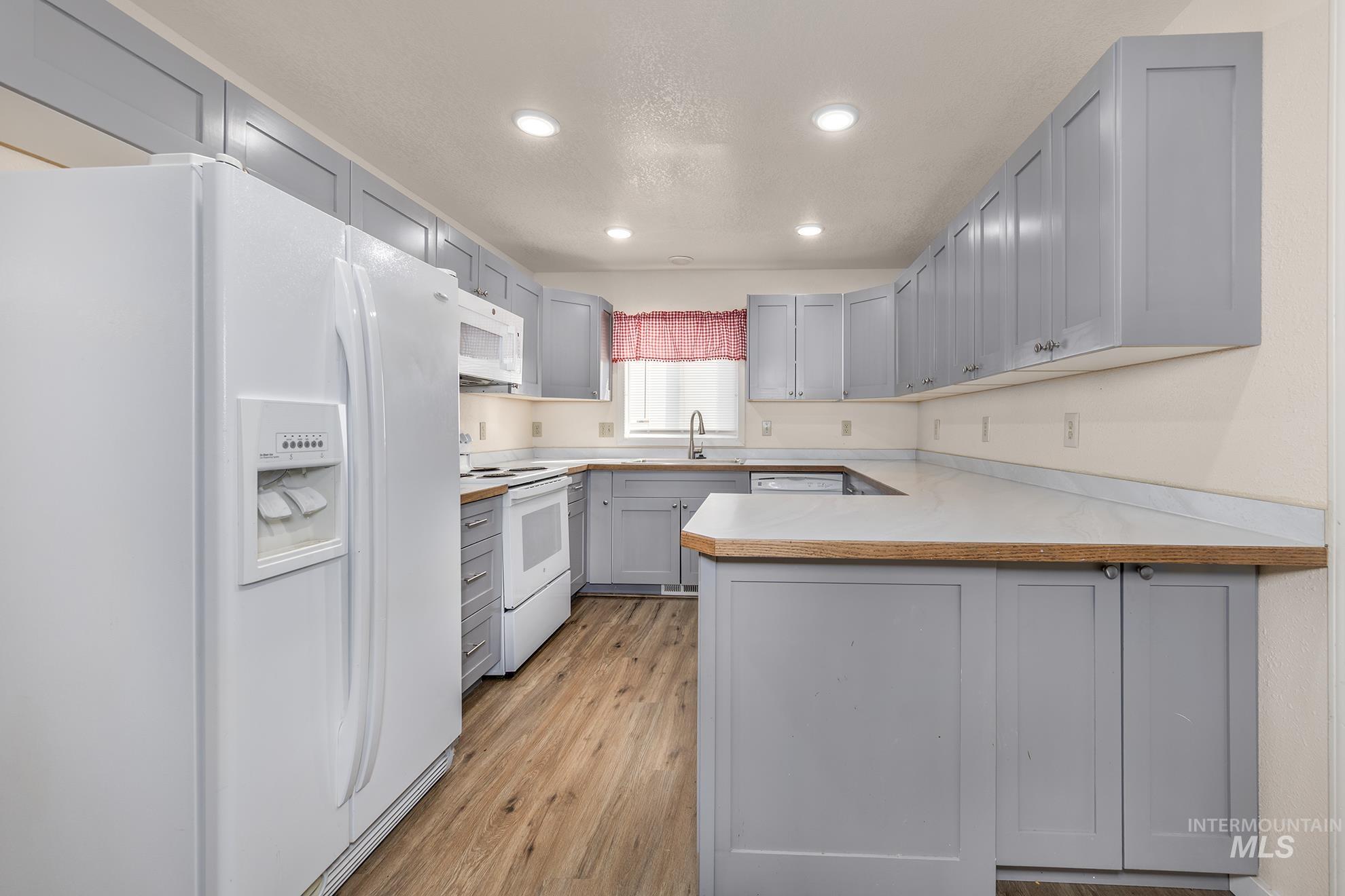 Kitchen with white appliances, a peninsula, light countertops, recessed lighting, and light wood-style flooring
