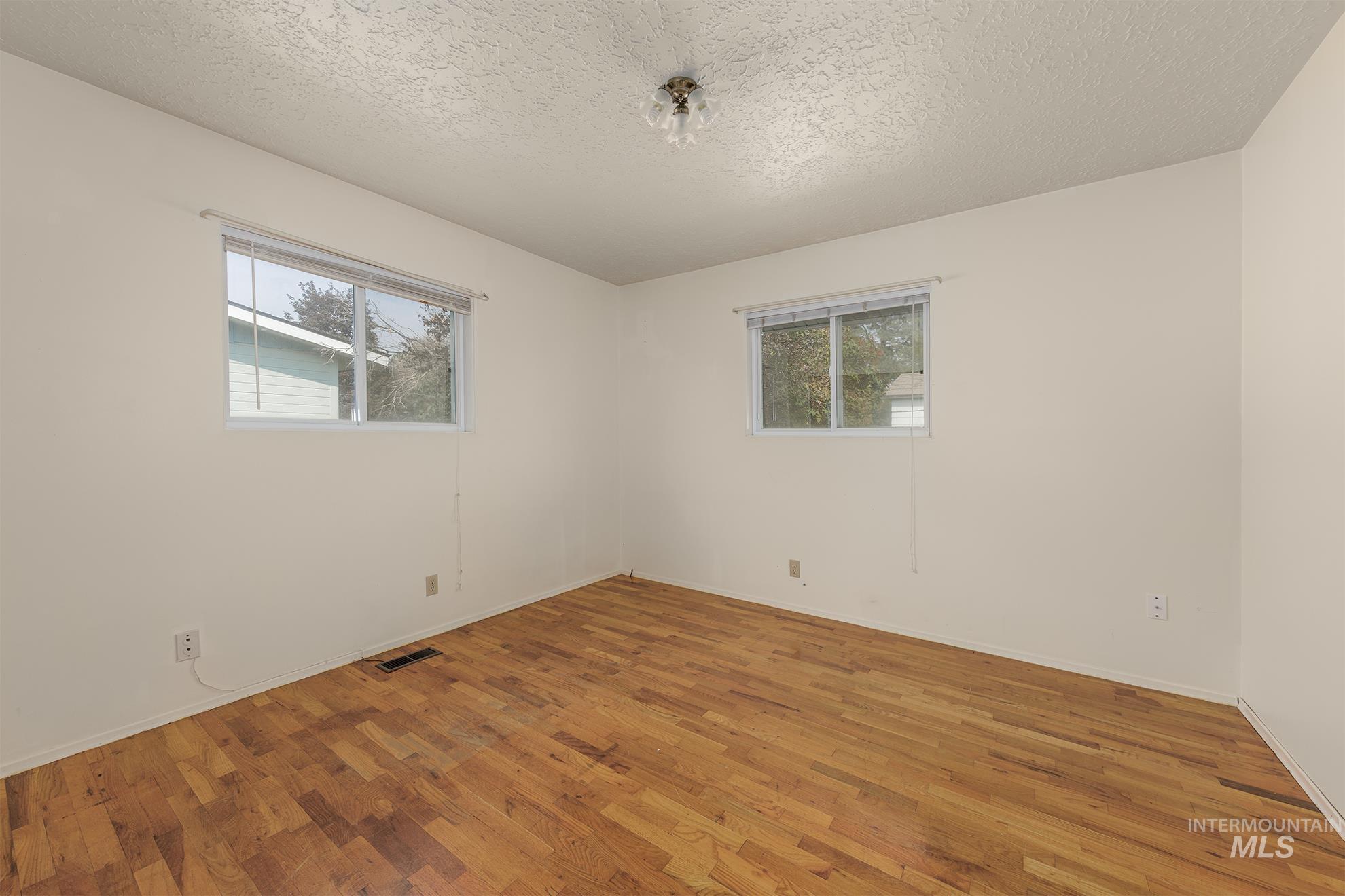 Empty room featuring healthy amount of natural light, wood finished floors, and a textured ceiling