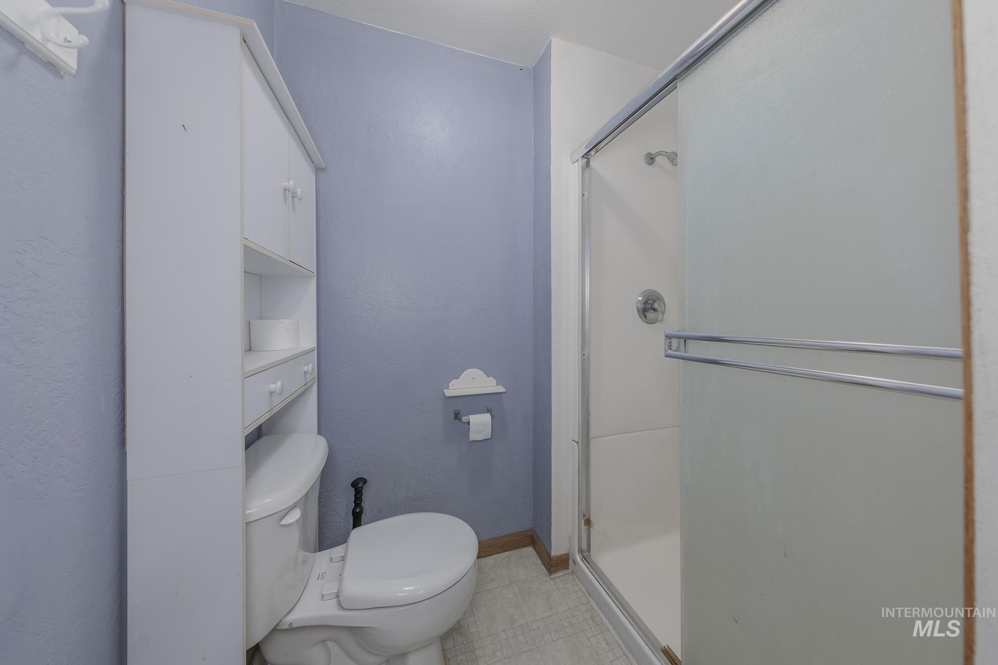 Bathroom featuring a stall shower, a textured wall, and light tile patterned floors