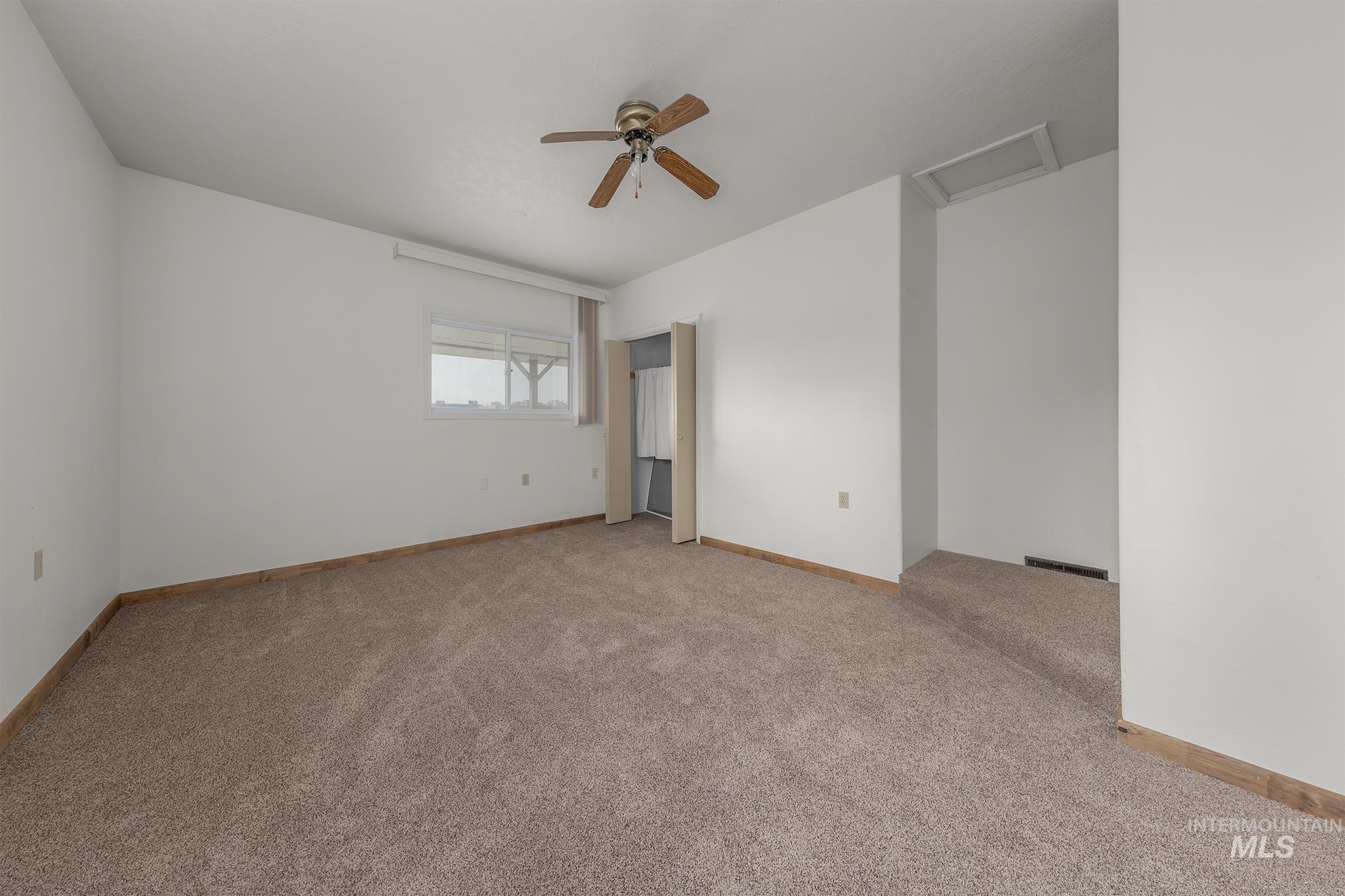 Unfurnished bedroom featuring attic access, light carpet, and a ceiling fan