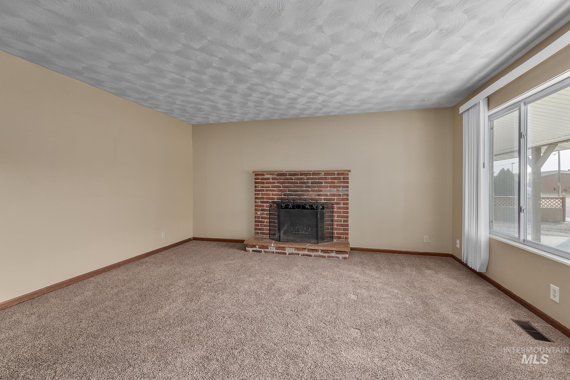 Unfurnished living room with a fireplace, carpet flooring, and a textured ceiling