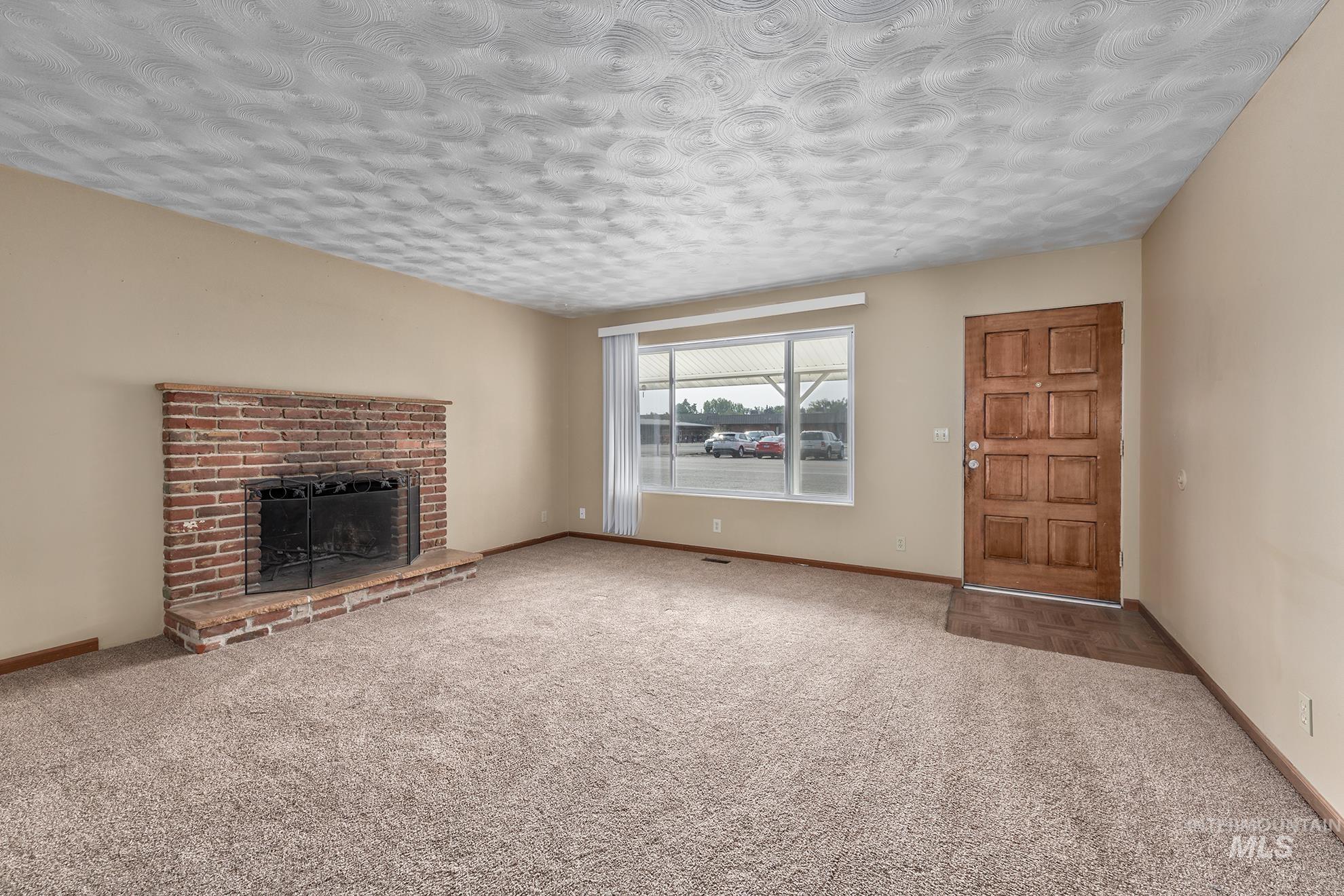 Unfurnished living room featuring a fireplace, carpet flooring, and a textured ceiling