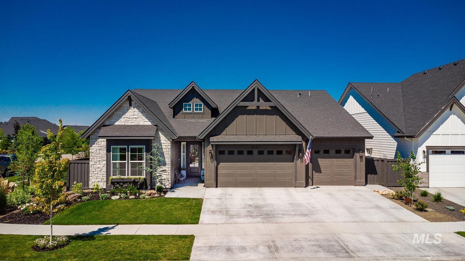 View of front facade with board and batten siding, an attached garage, driveway, and stone siding