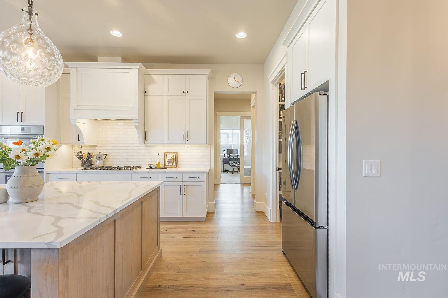 Kitchen with stainless steel appliances, light wood finished floors, white cabinetry, backsplash, and recessed lighting