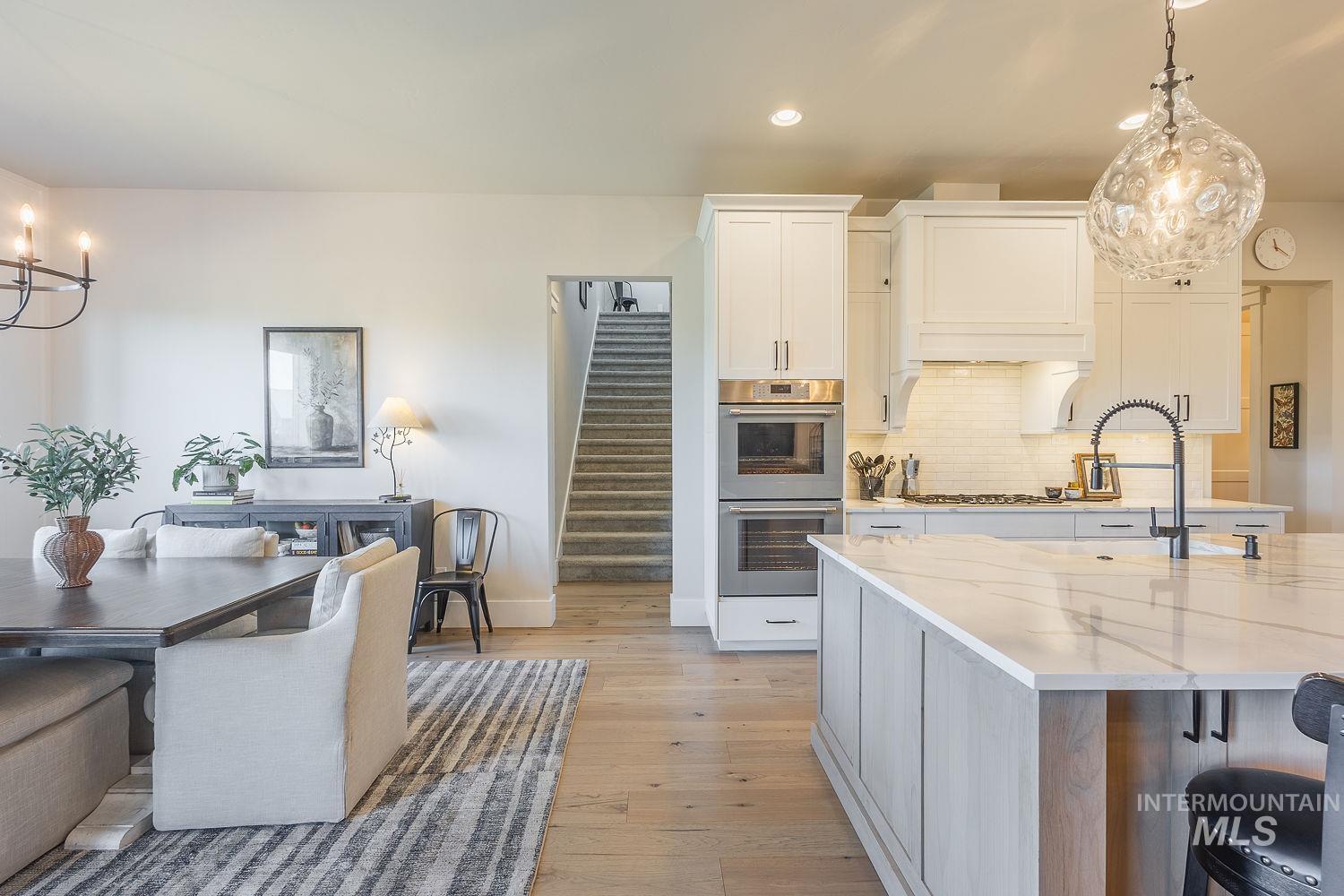 Kitchen with stainless steel double oven, recessed lighting, light wood-type flooring, white cabinetry, and backsplash
