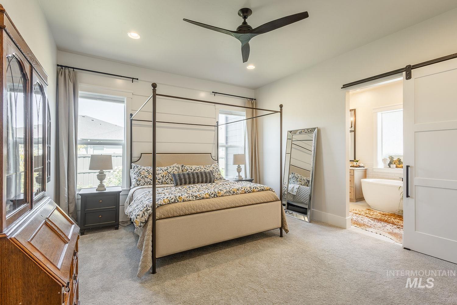 Carpeted bedroom with multiple windows, a barn door, ensuite bath, recessed lighting, and a ceiling fan
