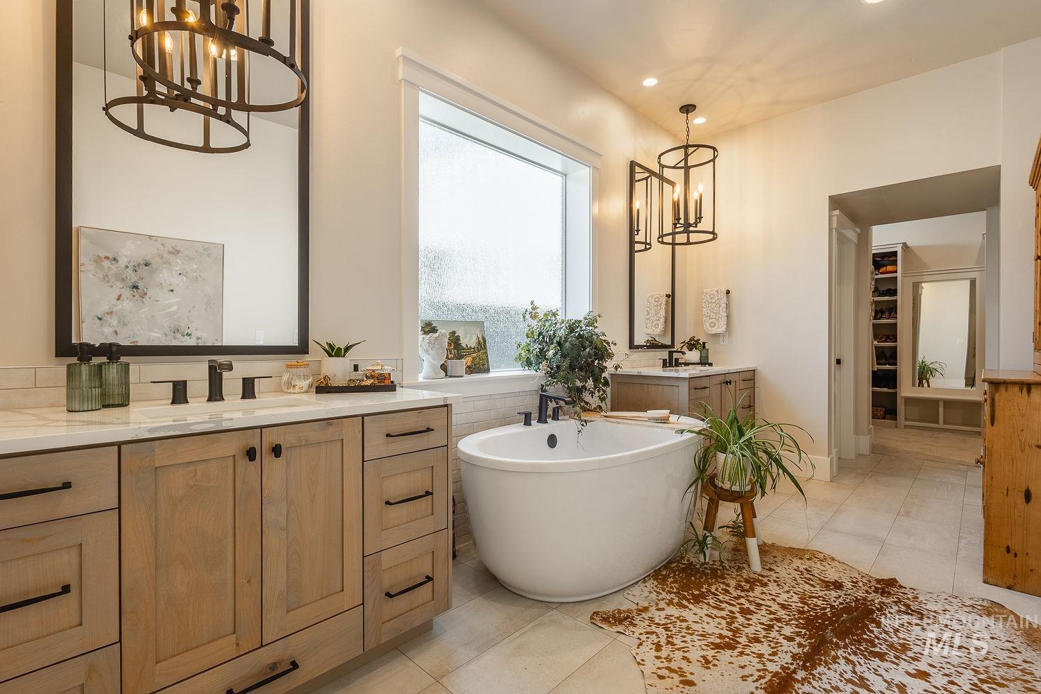 Bathroom with a chandelier, two vanities, a freestanding tub, tile patterned floors, and a spacious closet
