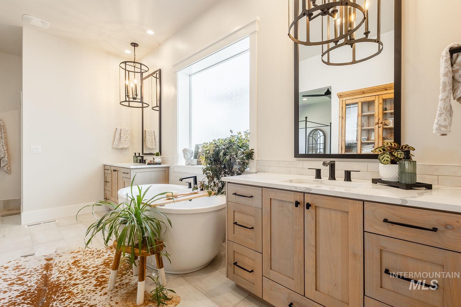 Bathroom featuring a chandelier, two vanities, a freestanding tub, and recessed lighting