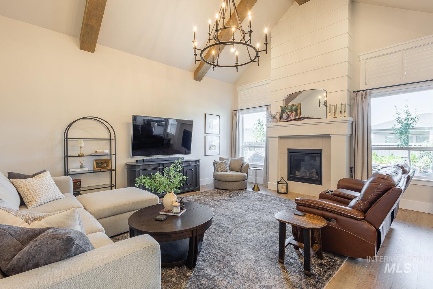 Living room with high vaulted ceiling, a fireplace, wood finished floors, a chandelier, and plenty of natural light