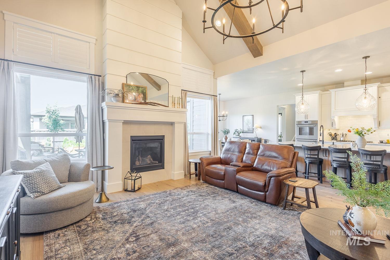 Living area featuring a chandelier, light wood-type flooring, high vaulted ceiling, plenty of natural light, and a tiled fireplace