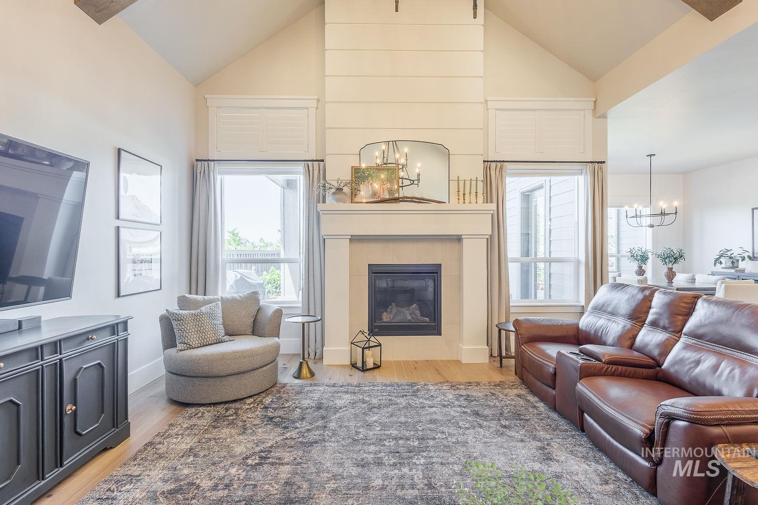 Living room with a chandelier, light wood-style flooring, high vaulted ceiling, and a tiled fireplace