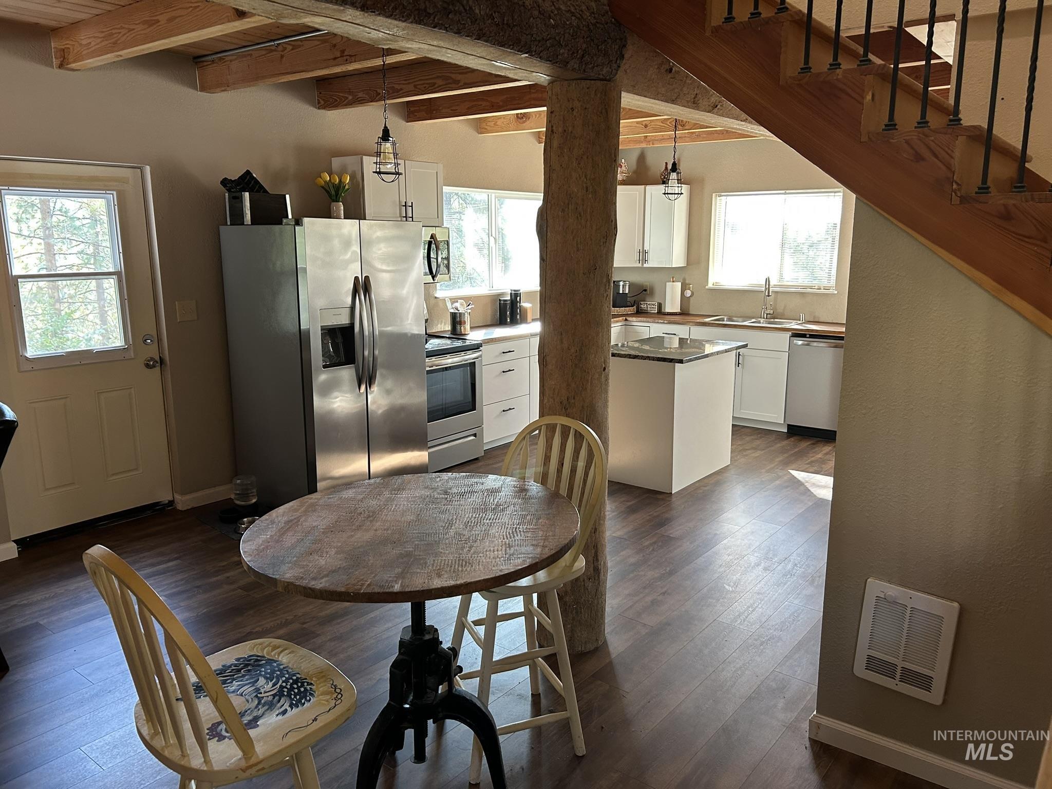 Kitchen featuring white cabinetry, appliances with stainless steel finishes, beamed ceiling, decorative light fixtures, and dark wood-style floors