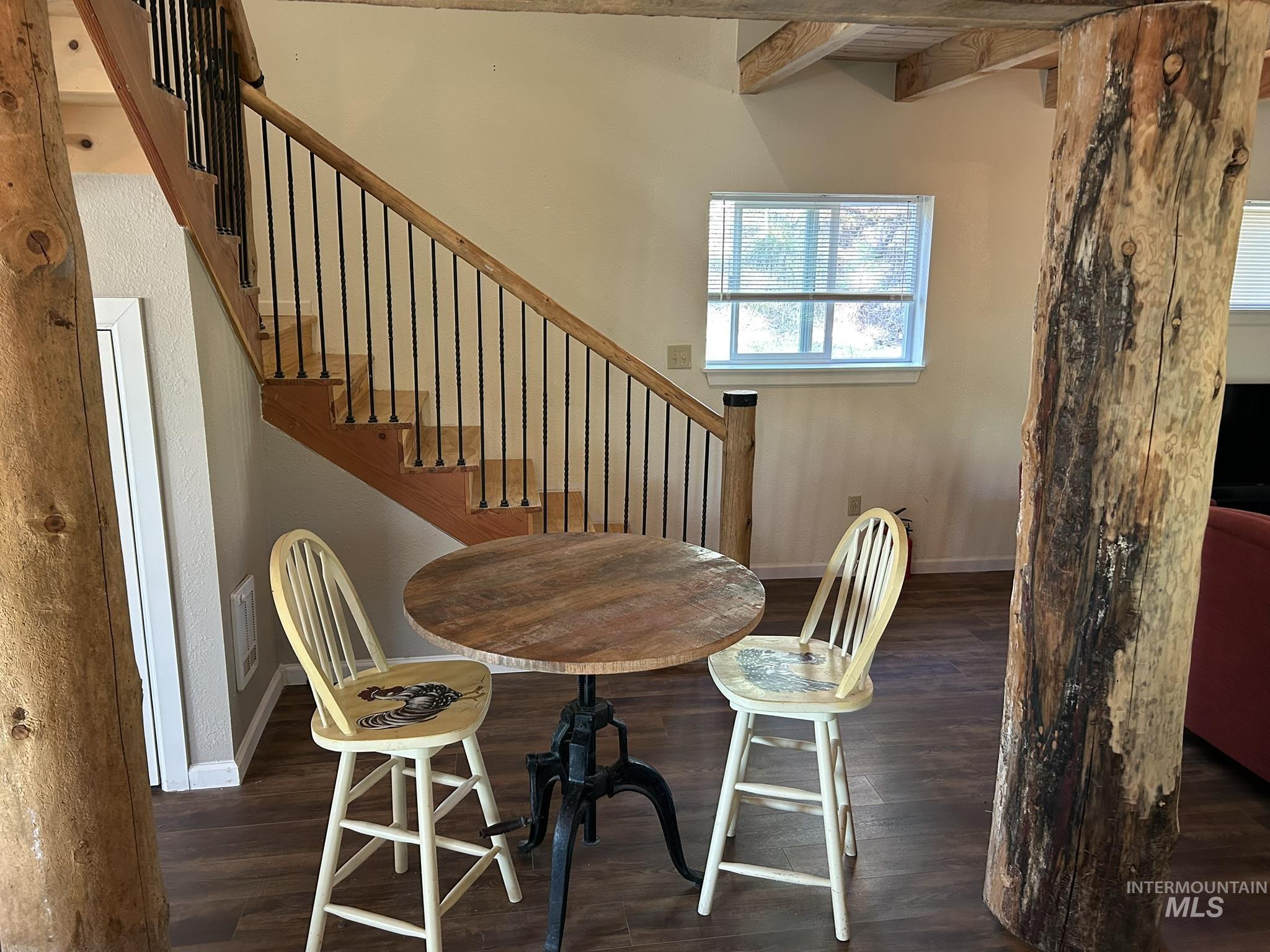 Dining space featuring beam ceiling, dark wood-style floors, and stairway