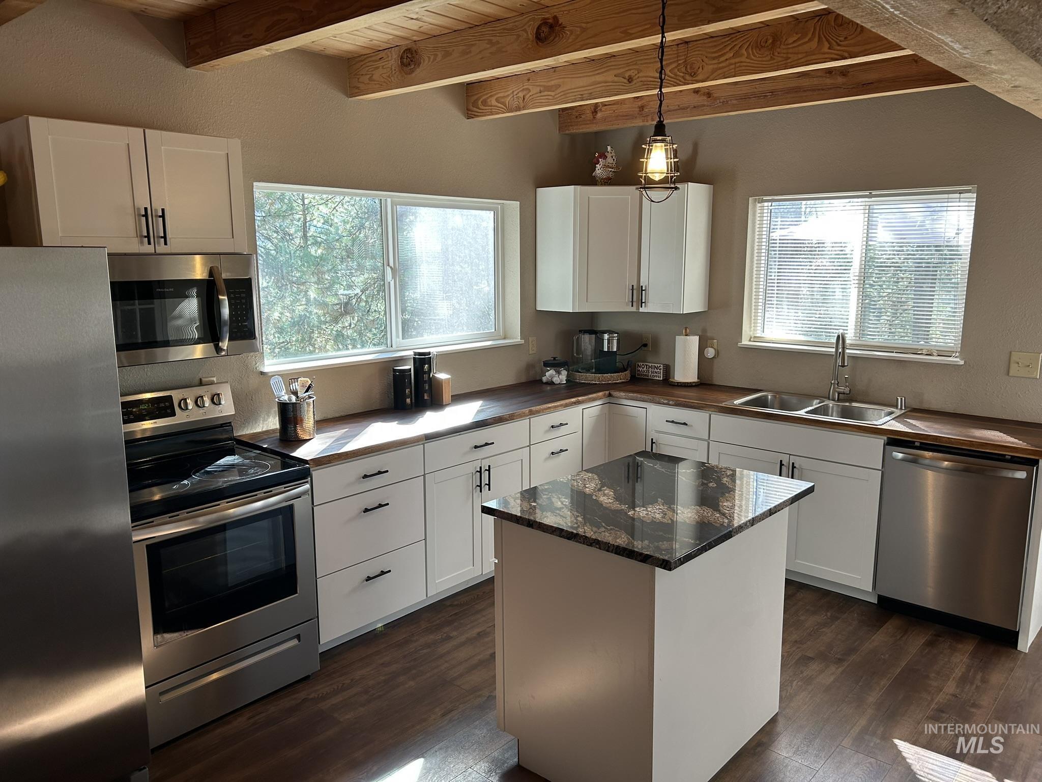 Kitchen with appliances with stainless steel finishes, dark wood finished floors, a kitchen island, white cabinets, and a wooden ceiling with exposed beams