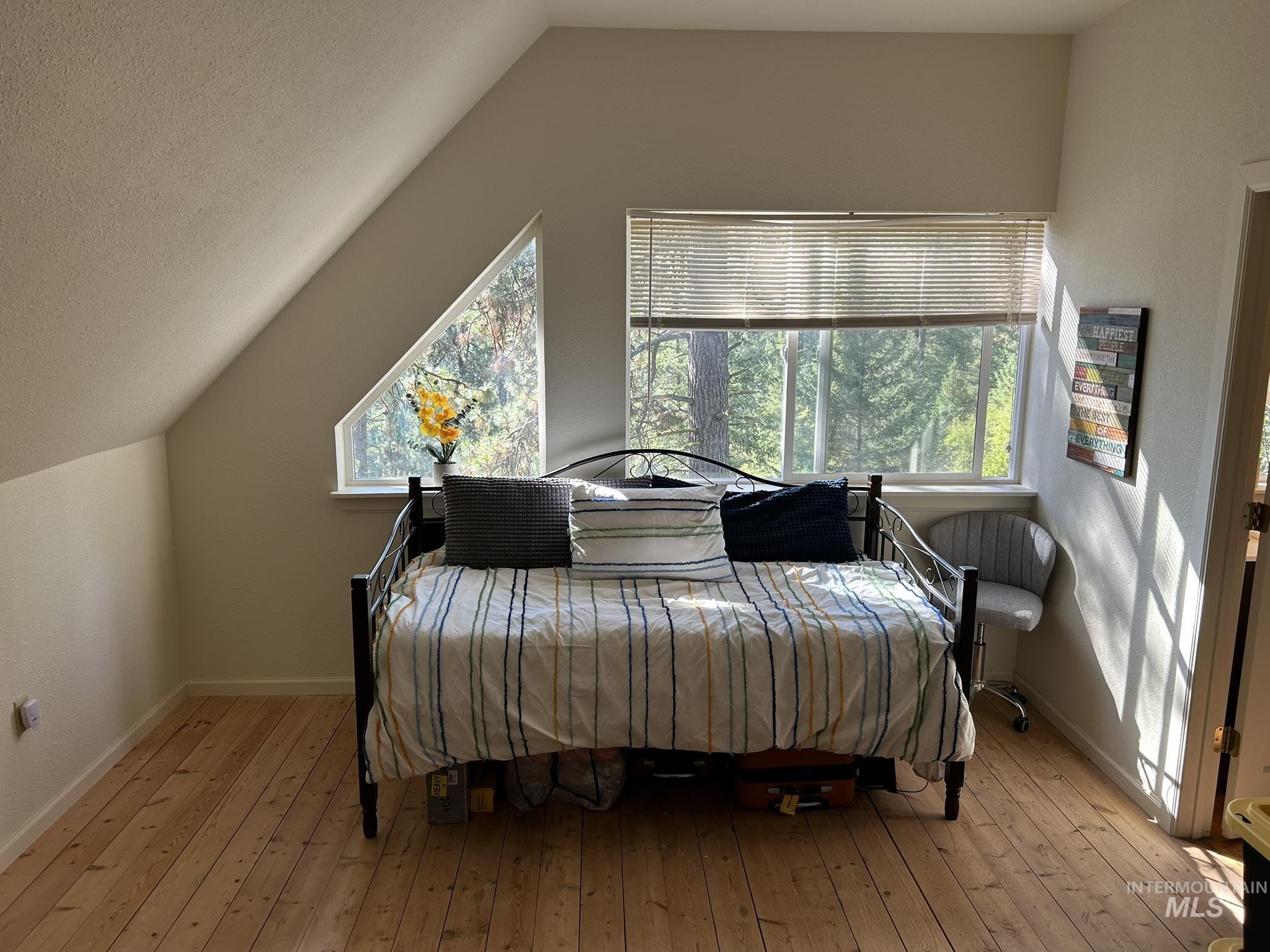 Bedroom with multiple windows, lofted ceiling, and light wood finished floors