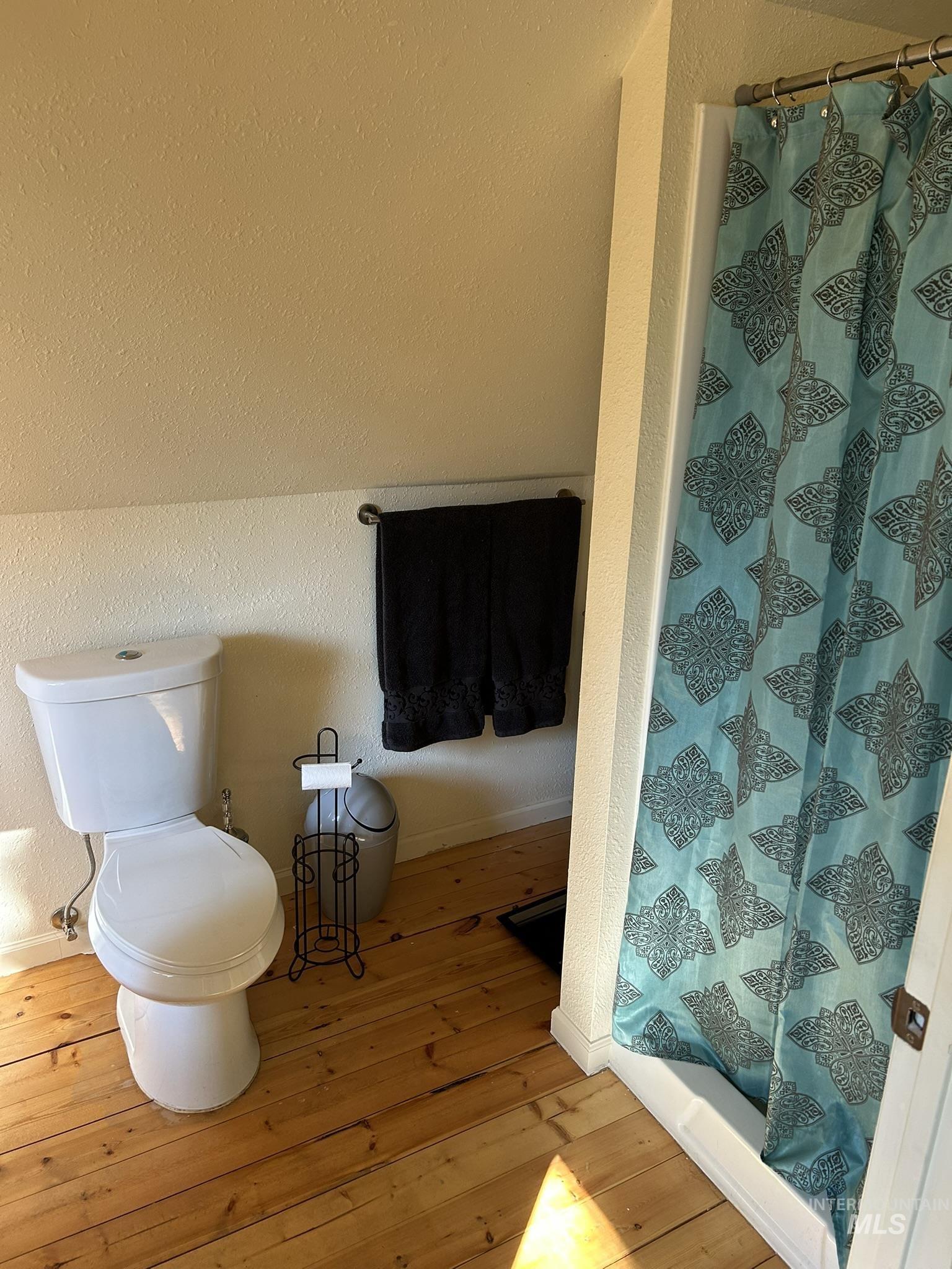 Full bath featuring a textured wall, a stall shower, and light wood-style flooring