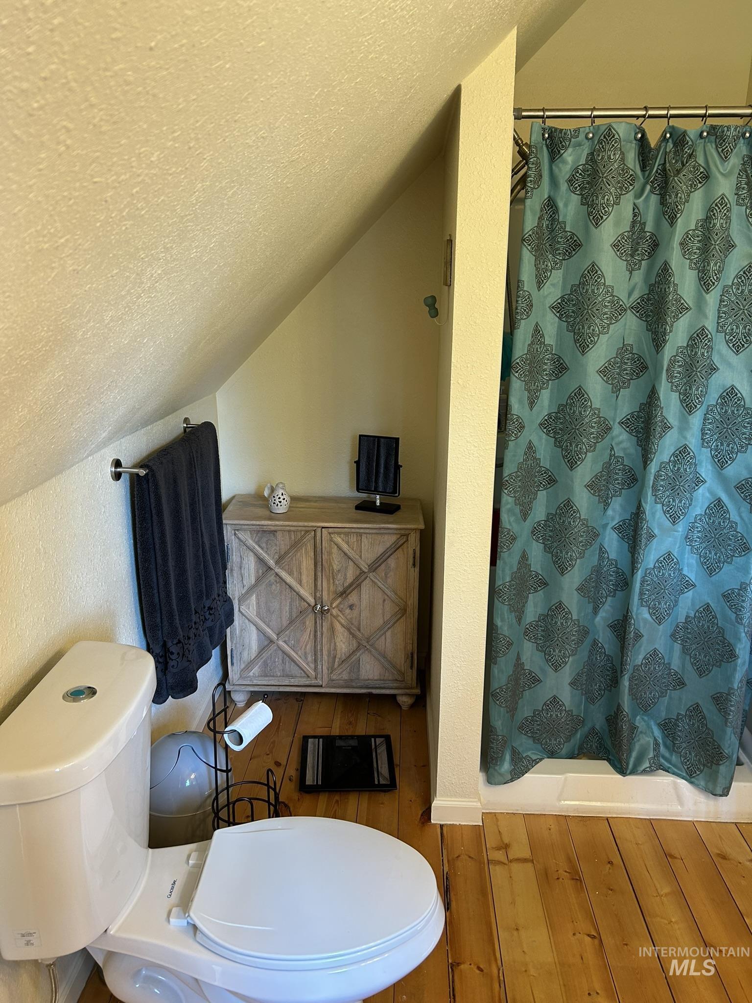 Full bath with a textured ceiling, lofted ceiling, a stall shower, hardwood / wood-style floors, and a textured wall