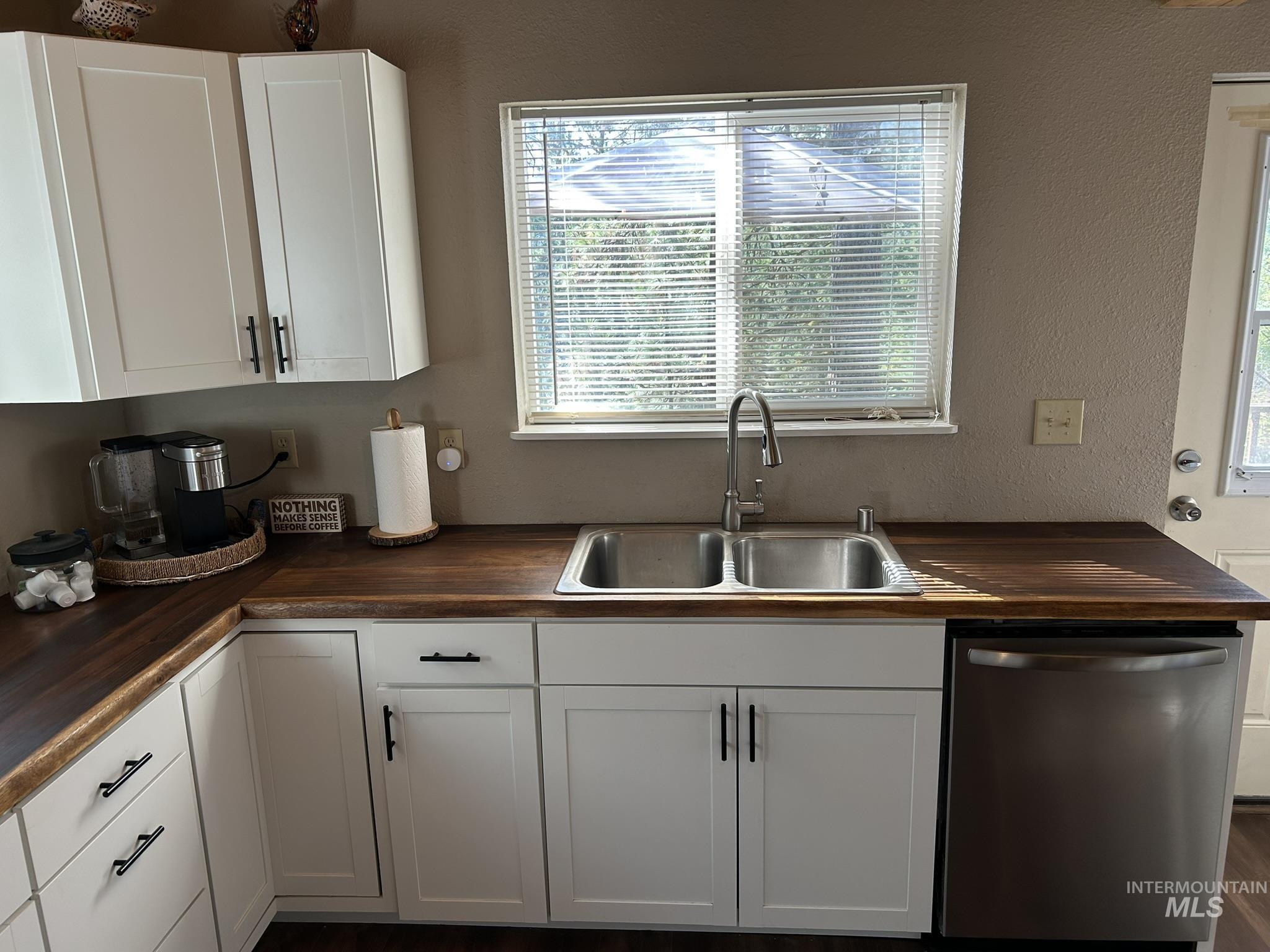 Kitchen with white cabinets, dishwasher, a textured wall, and butcher block counters