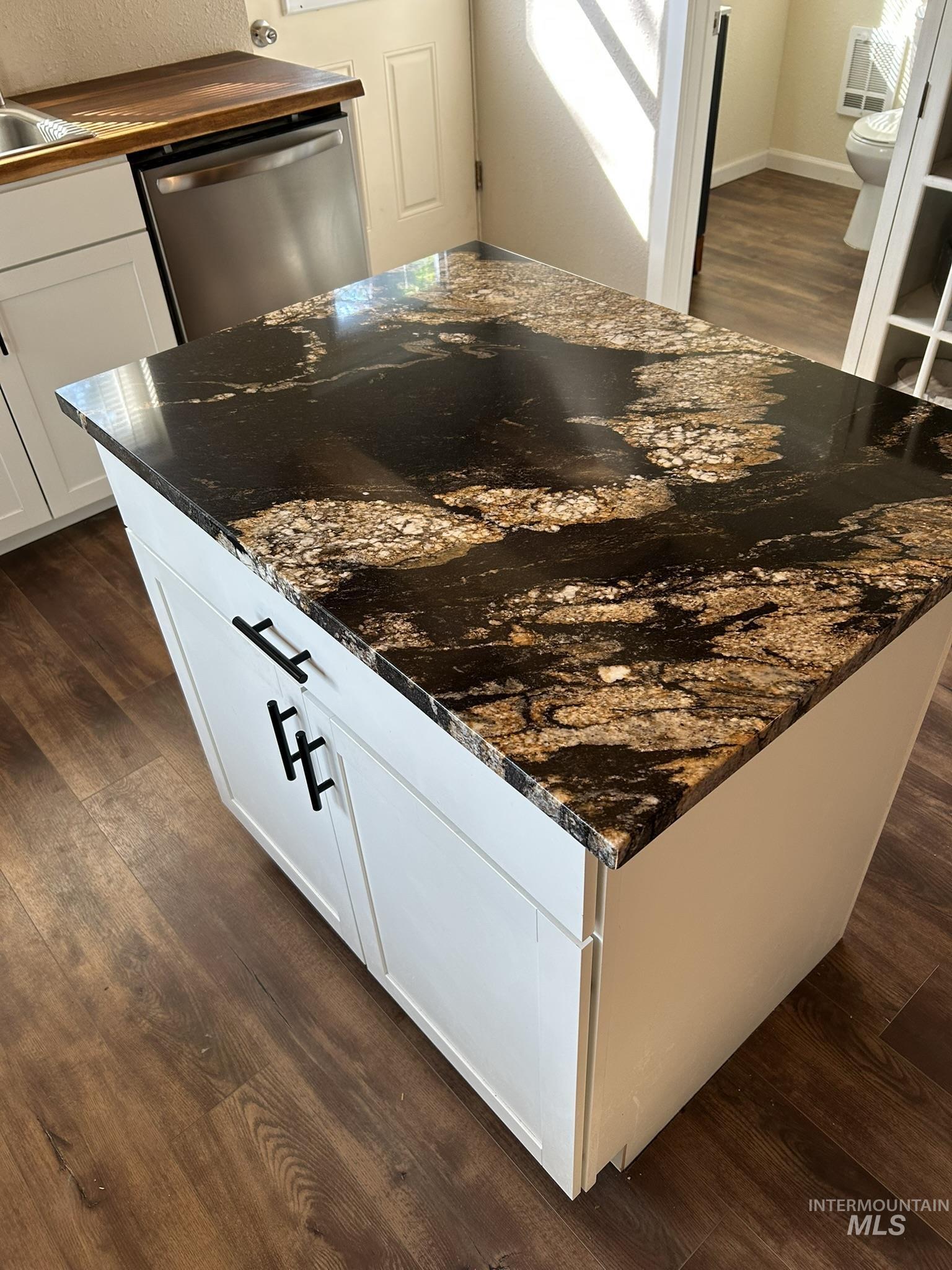 Kitchen view of dark wood-type flooring, dishwasher, white cabinetry, a center island, and dark stone counters