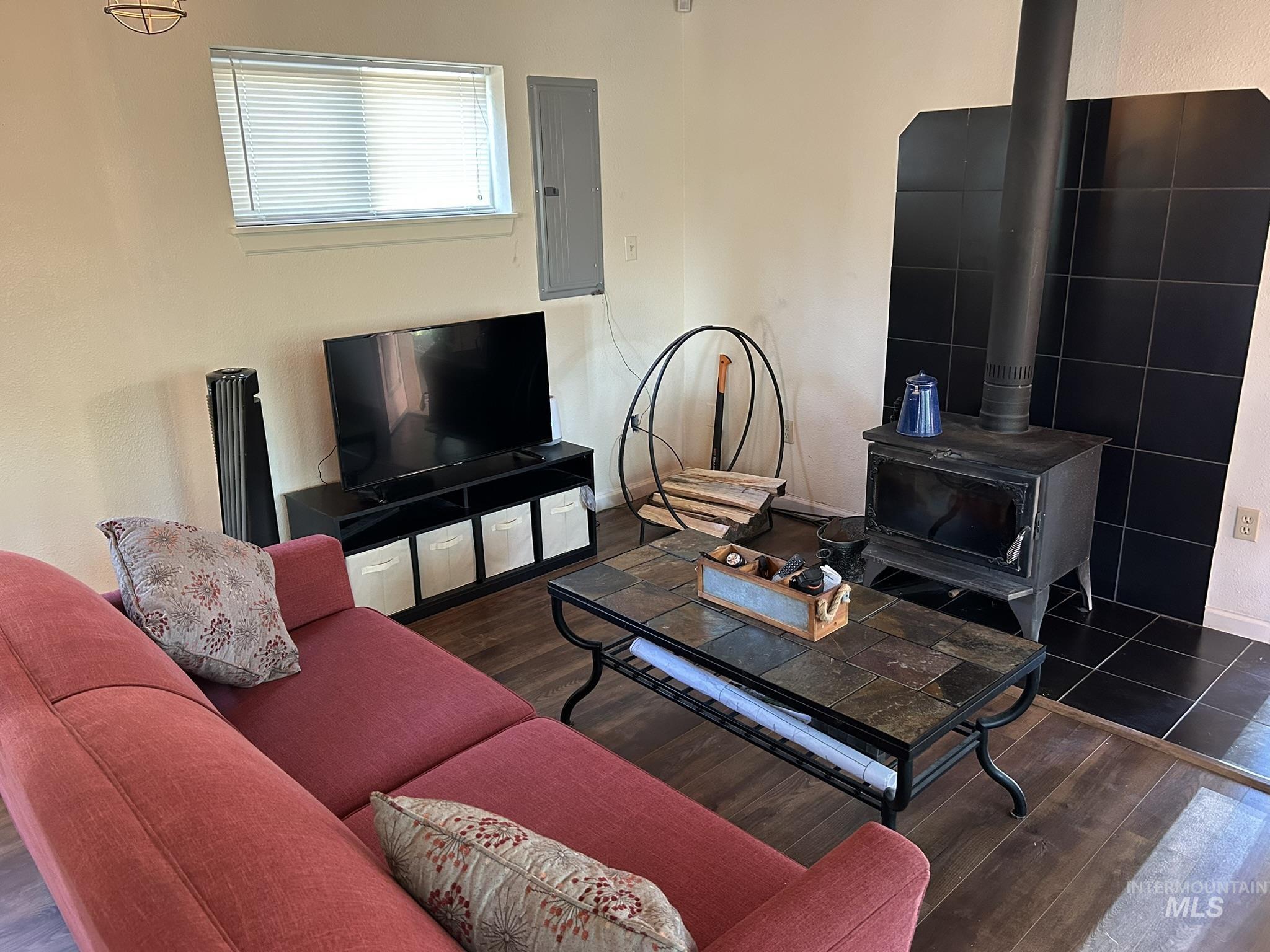 Living room featuring a wood stove, electric panel, wood finished floors, and a textured wall