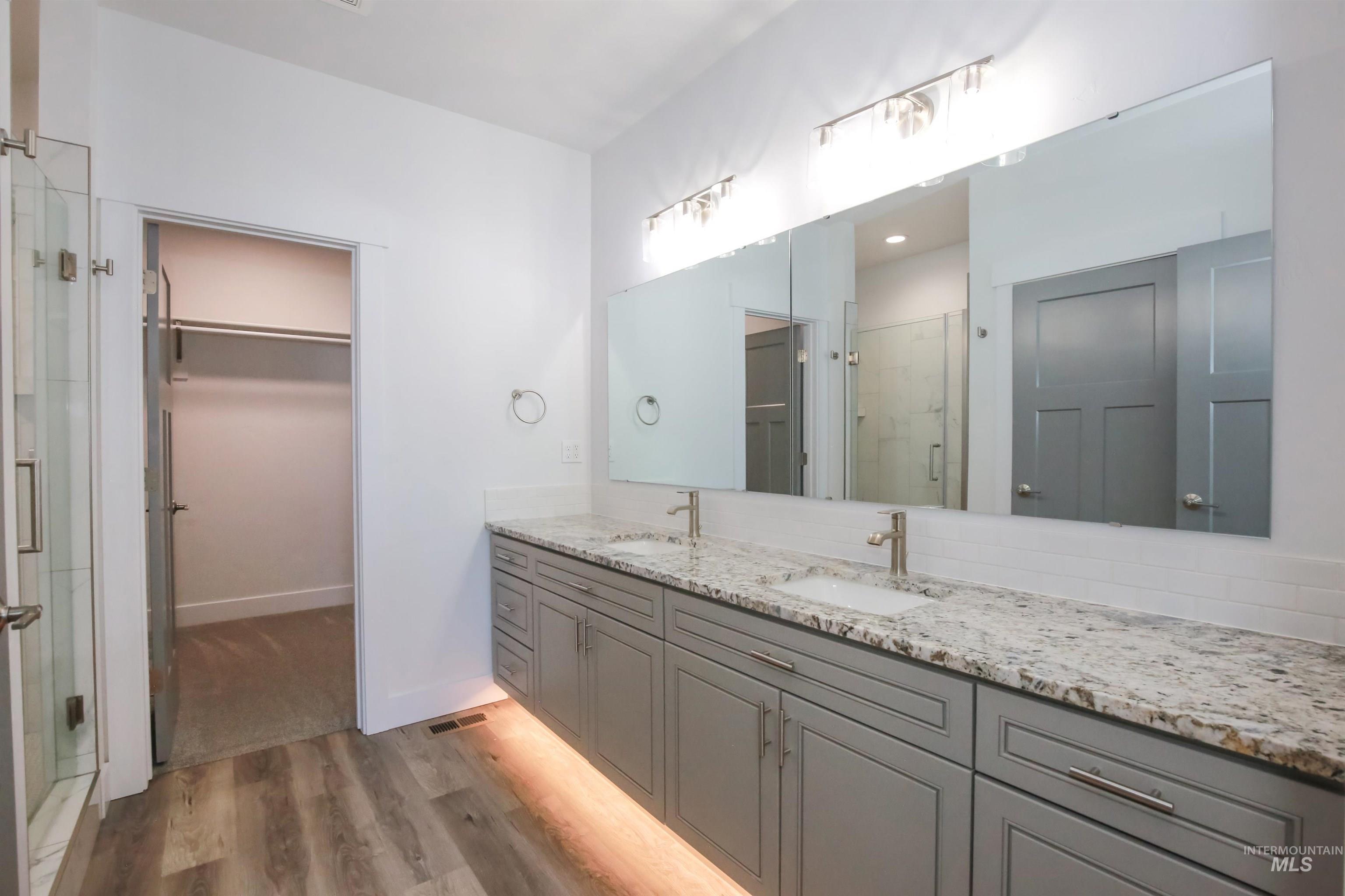 Bathroom with double vanity, a shower stall, light wood-style flooring, and a spacious closet