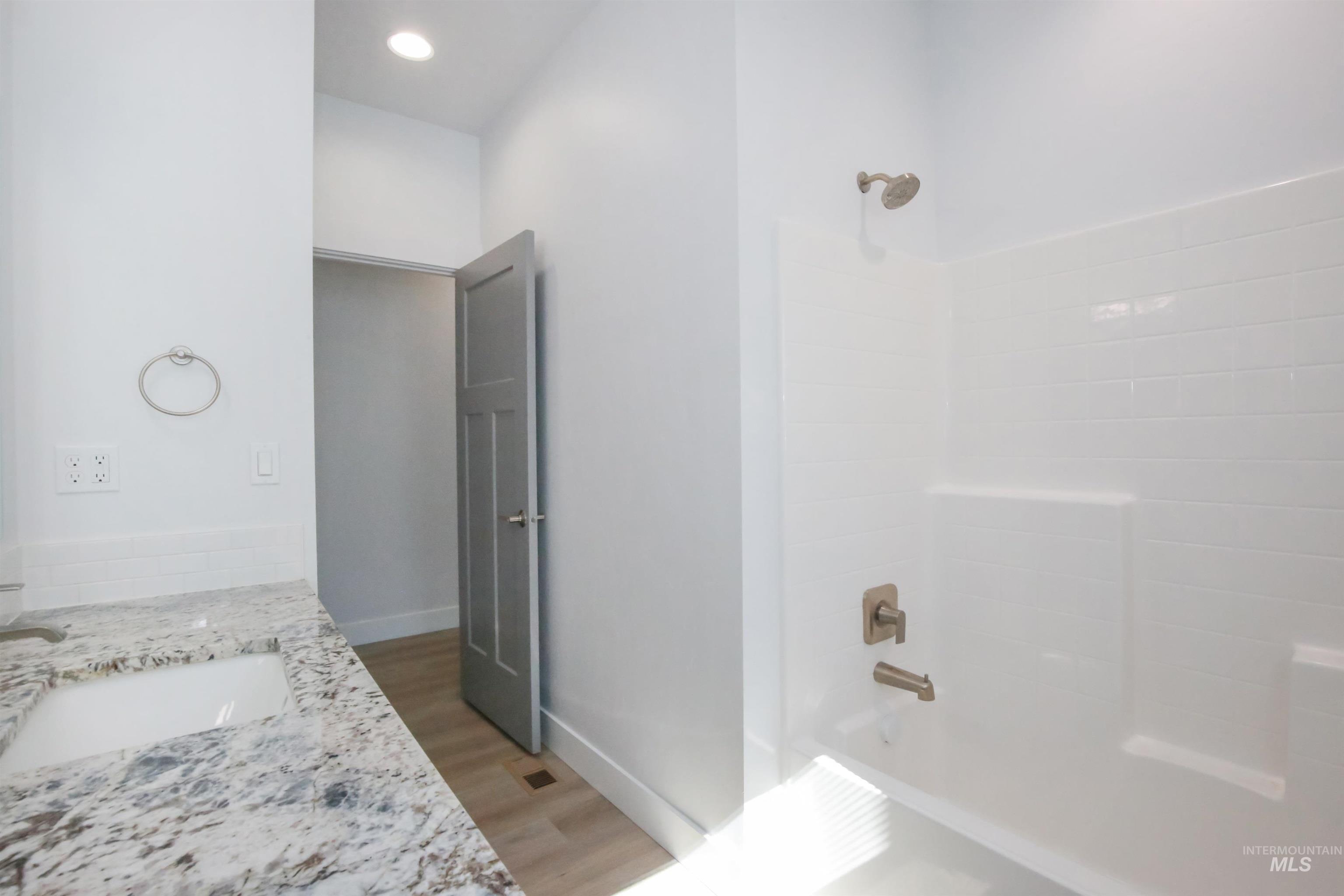 Bathroom with washtub / shower combination, light wood finished floors, double vanity, and recessed lighting