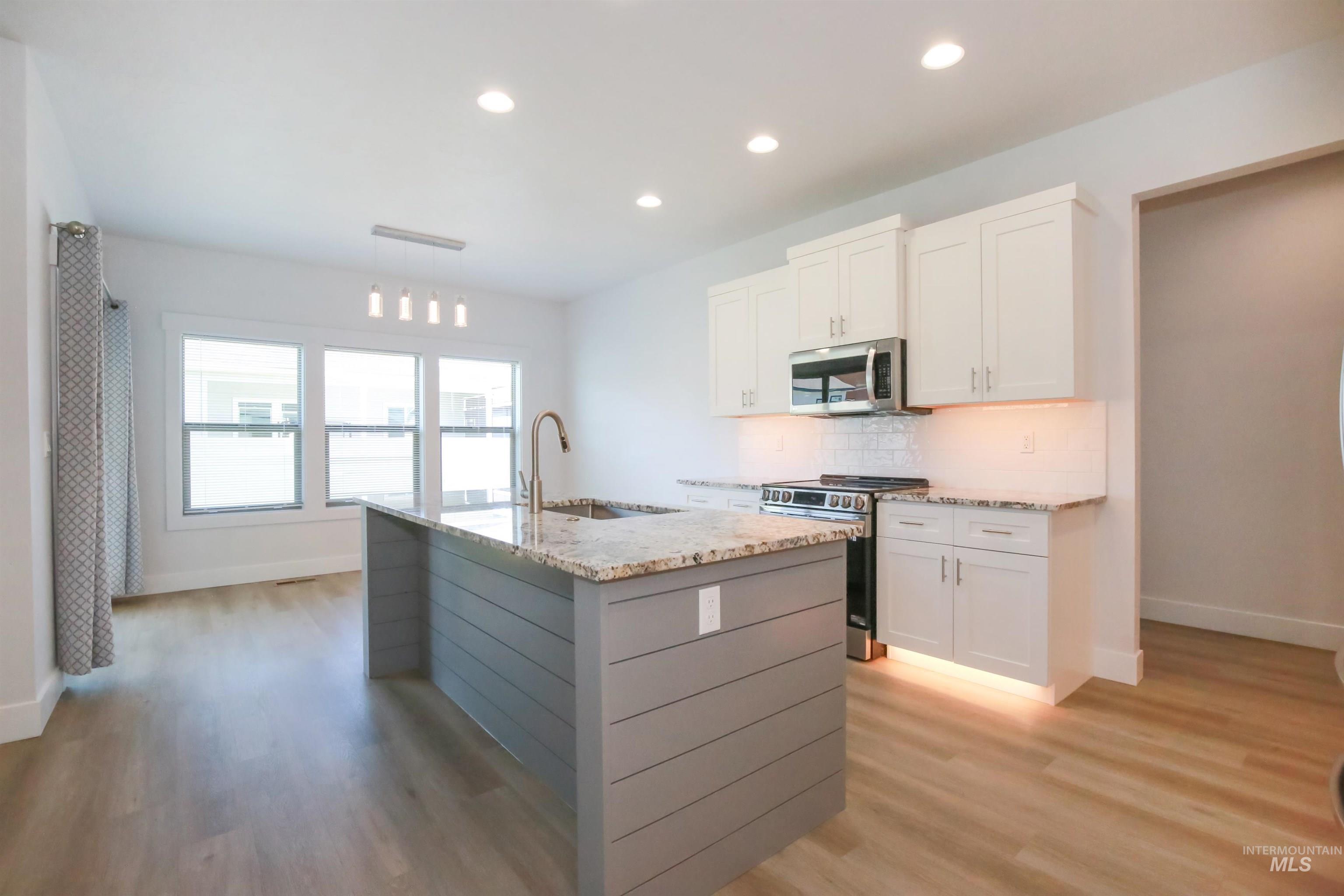 Kitchen with stainless steel appliances, white cabinetry, backsplash, a center island with sink, and light stone countertops