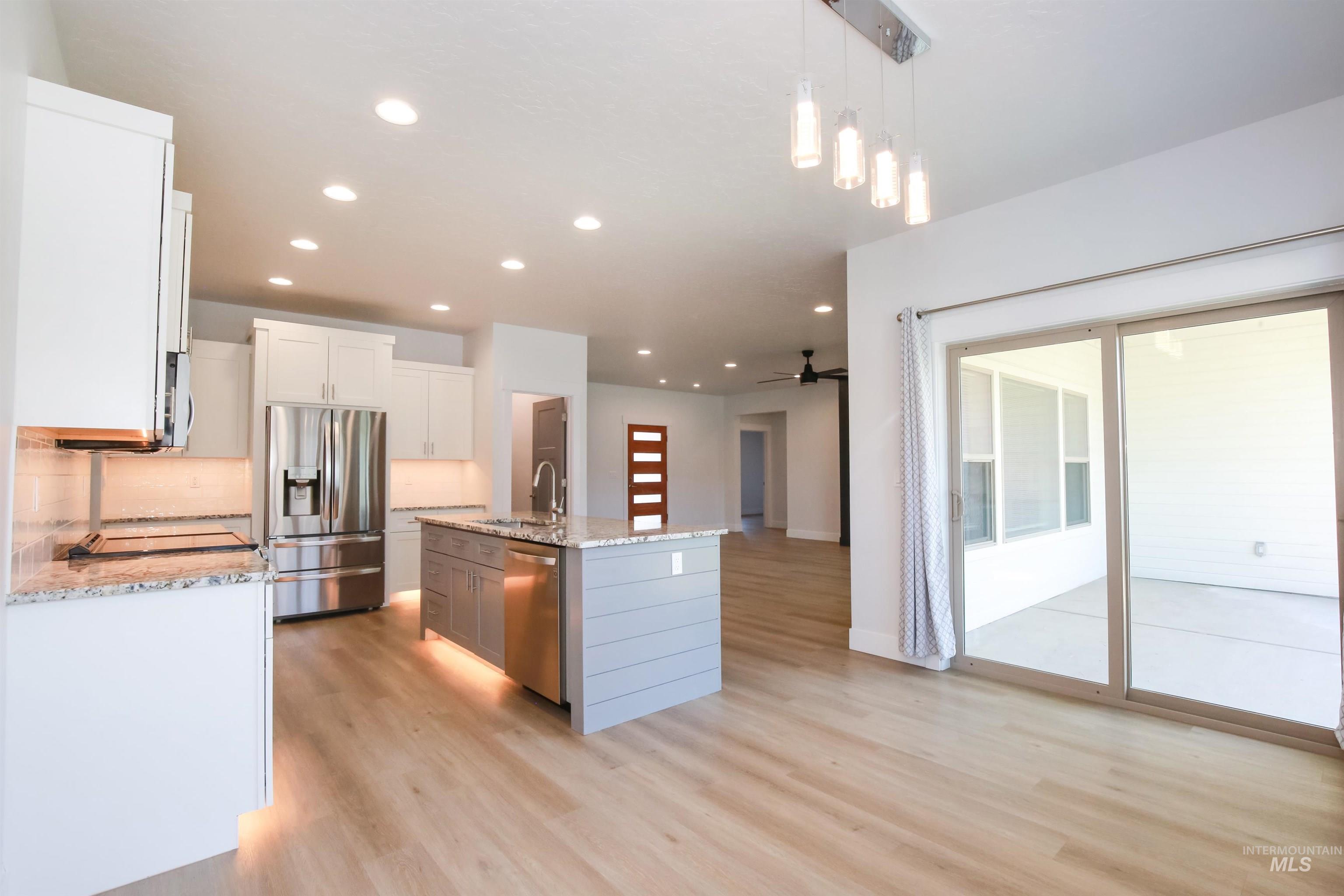 Kitchen featuring recessed lighting, appliances with stainless steel finishes, ceiling fan, light stone countertops, and decorative light fixtures