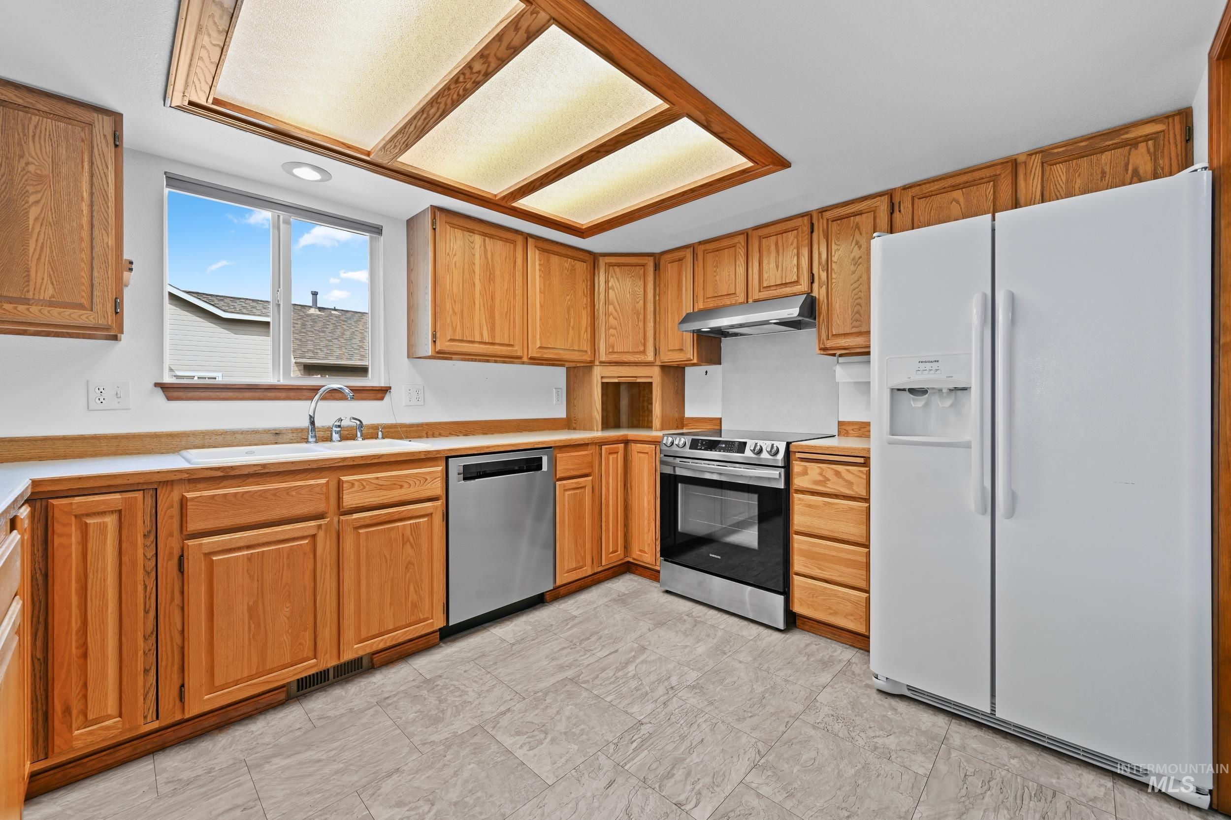 Kitchen with stainless steel appliances, light countertops, brown cabinetry, and under cabinet range hood