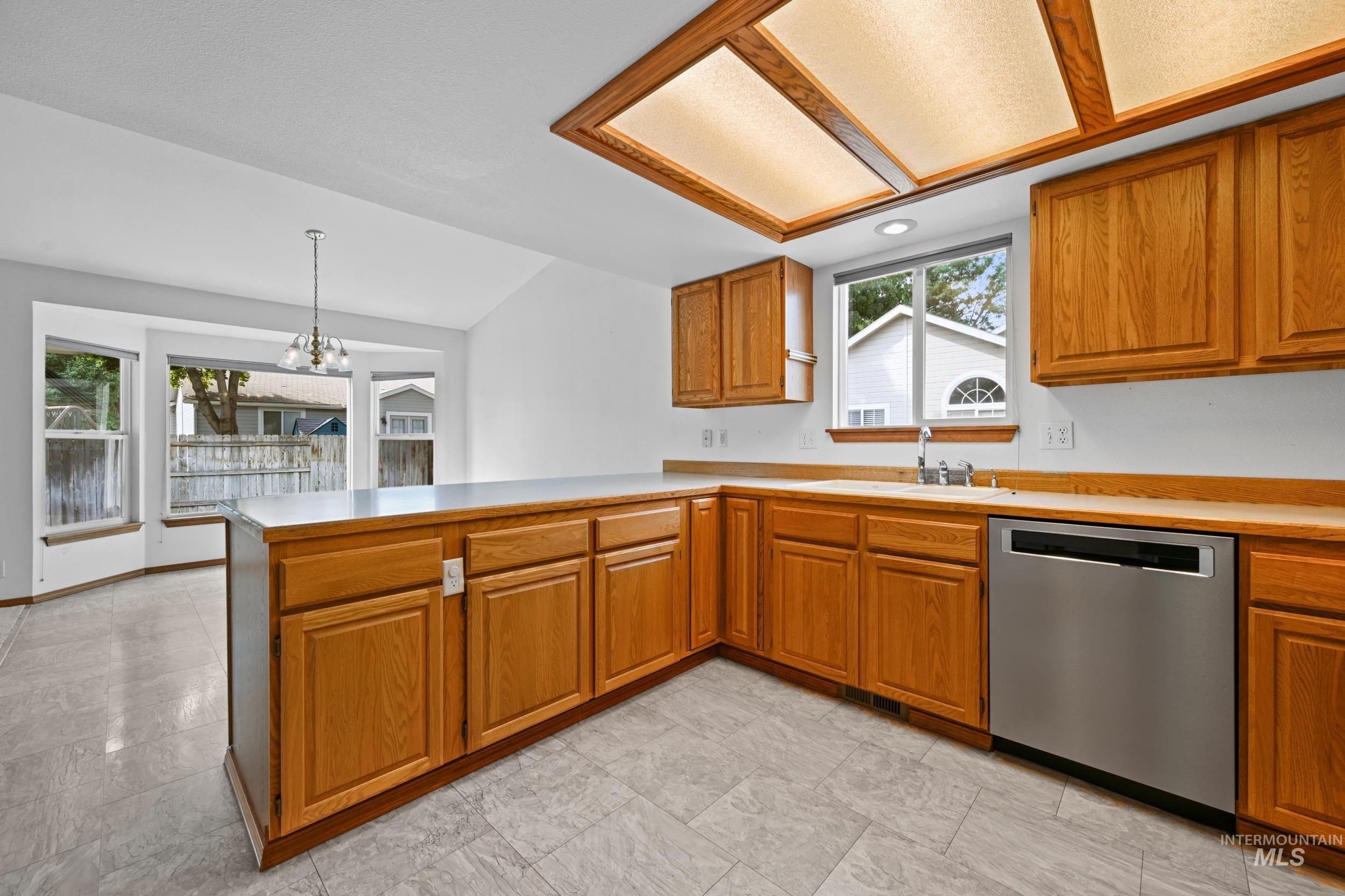 Kitchen with brown cabinetry, a peninsula, light countertops, stainless steel dishwasher, and lofted ceiling