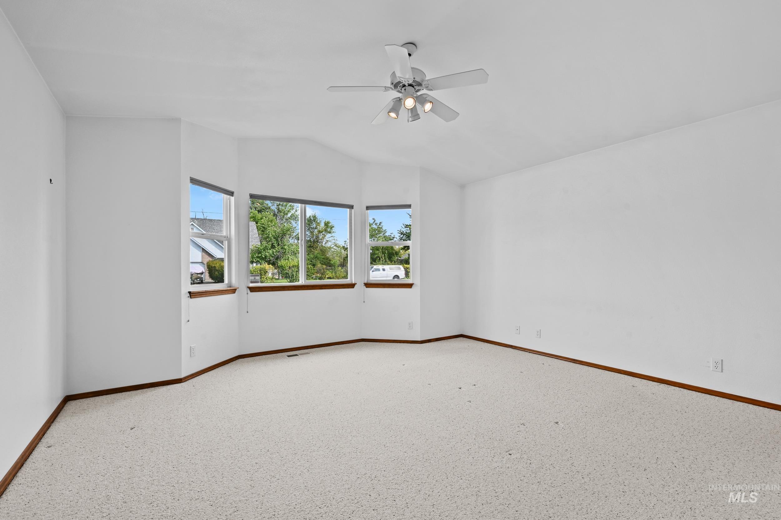 Carpeted spare room with a ceiling fan and vaulted ceiling