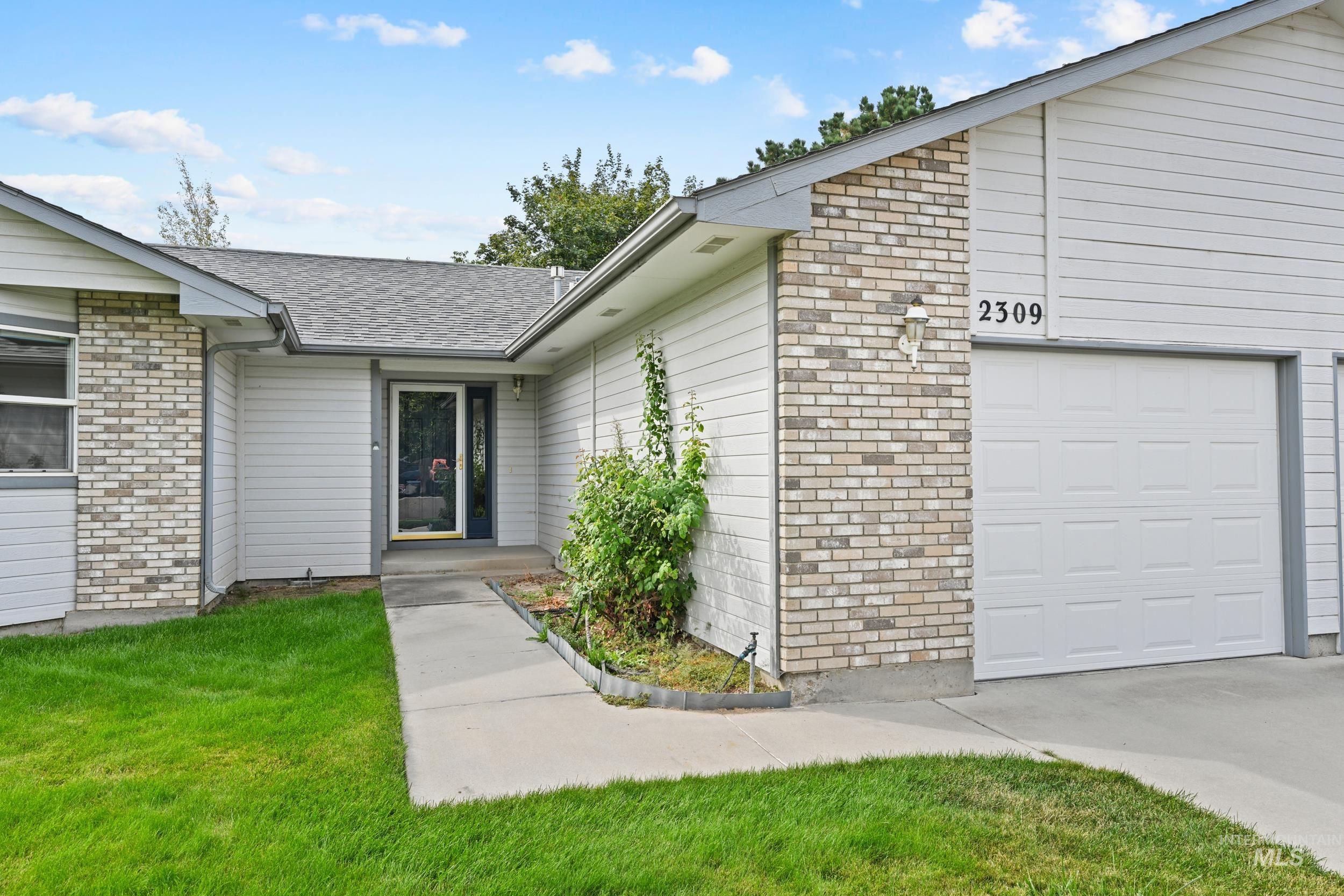 View of exterior entry featuring brick siding, roof with shingles, a garage, and a lawn