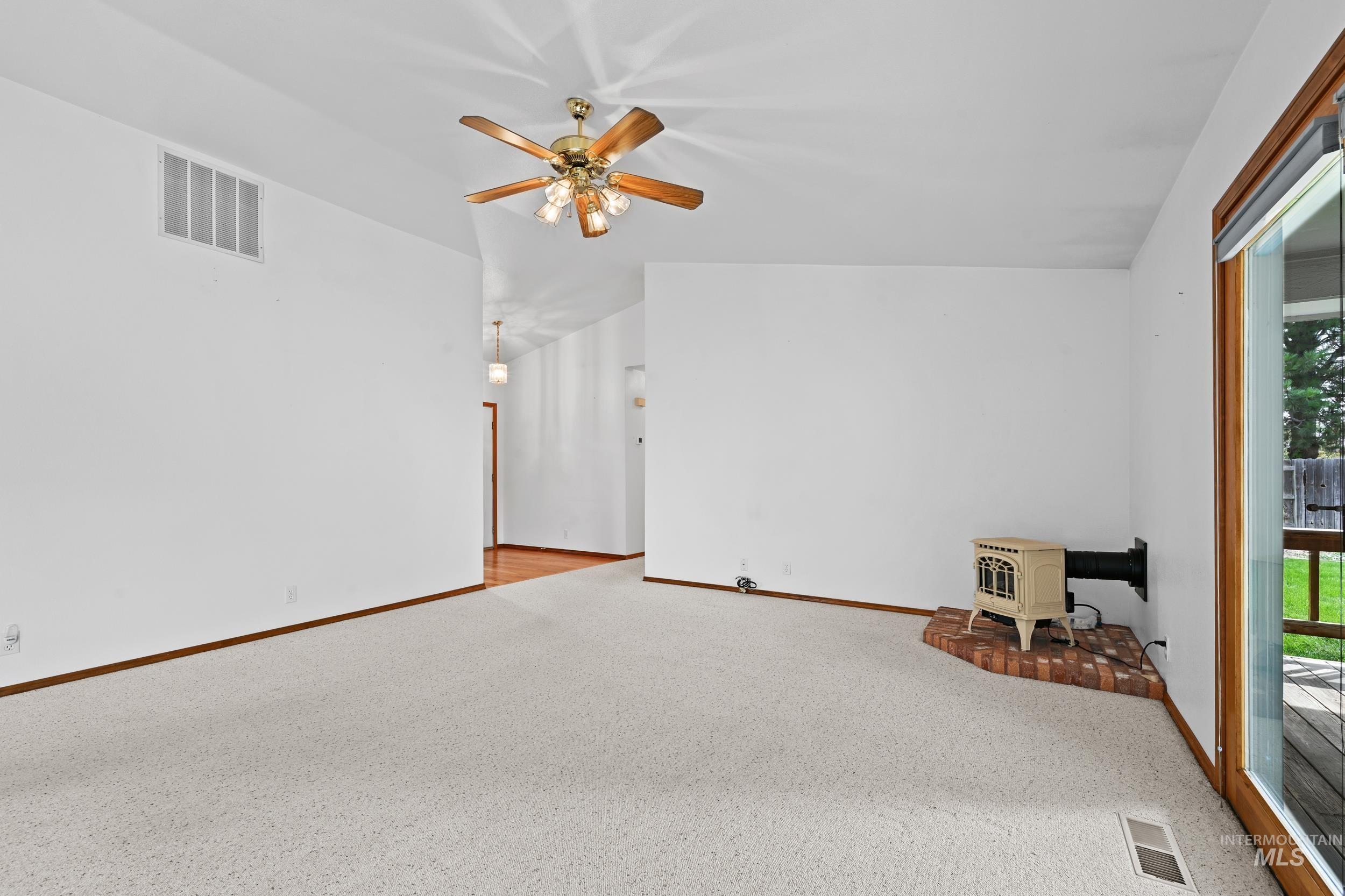 Carpeted spare room featuring a wood stove and ceiling fan